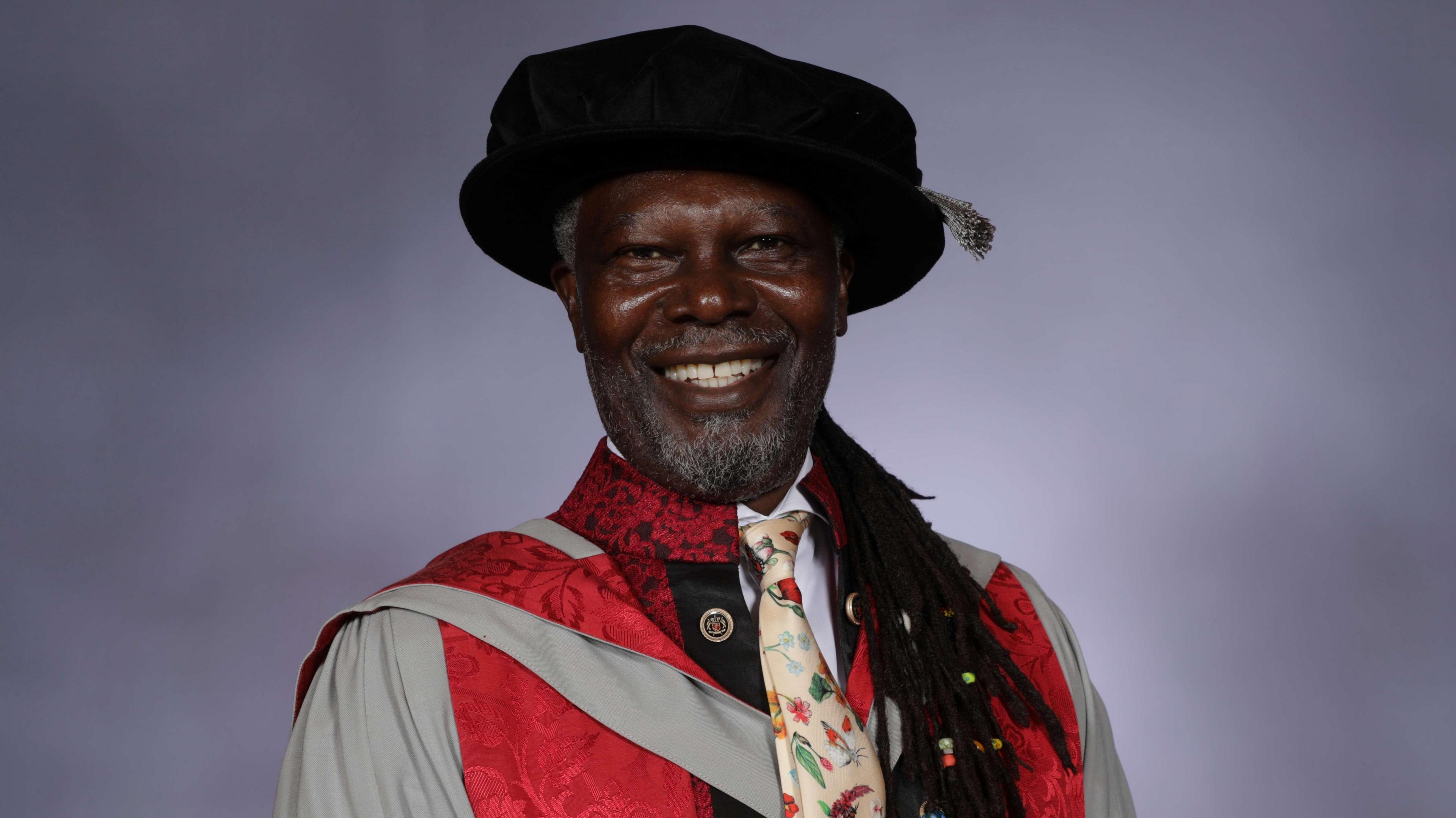 Levi Roots. He is pictured wearing a graduation cap and gown. He is smiling at the camera. 