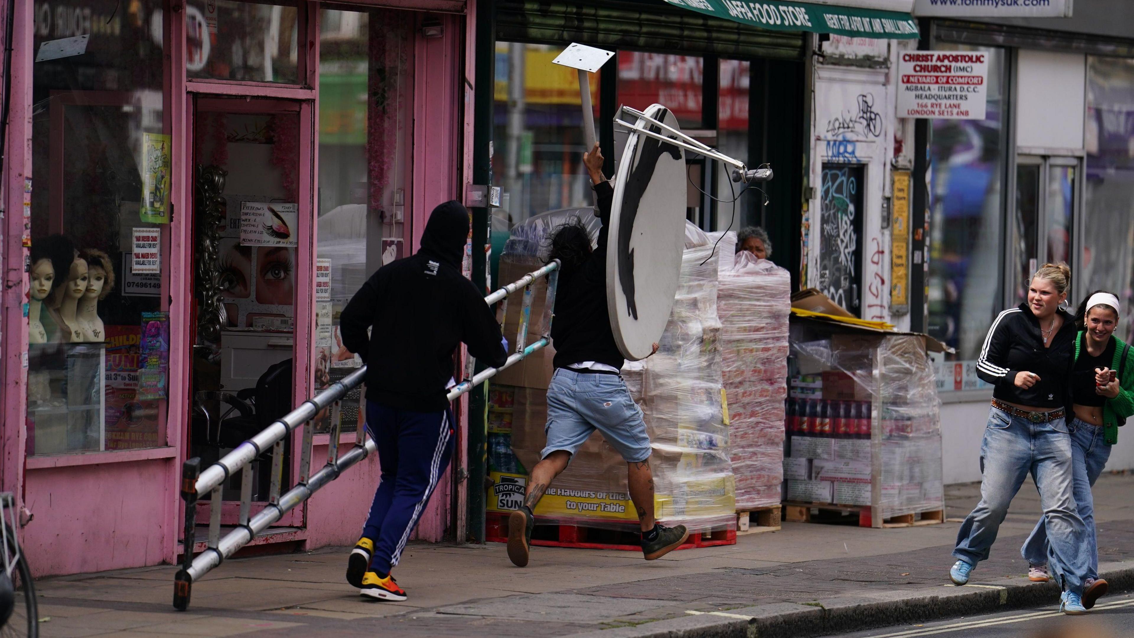 A man with a ladder and another with the satellite dish are seen running off down the high street with the Banksy.