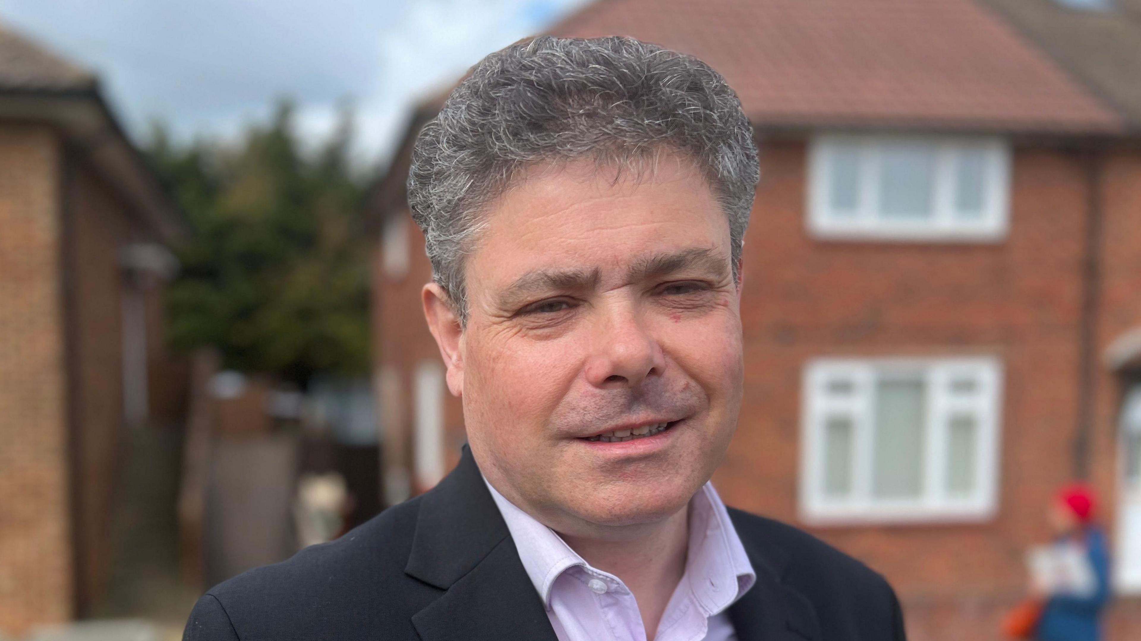 John Kent, wearing an open collar pink shirt and a dark-coloured suit jacket