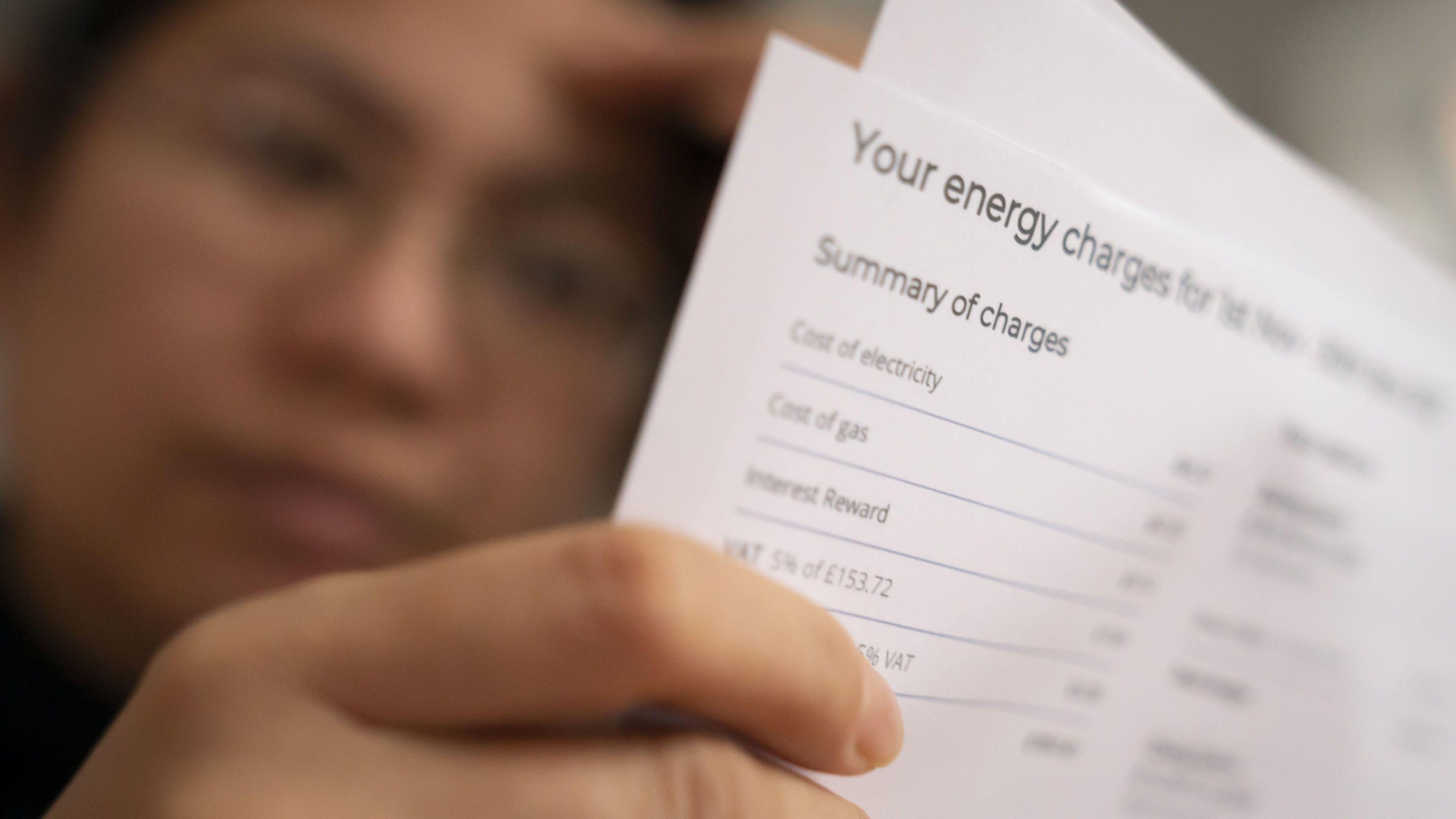 A woman examines the breakdown her energy bill, held in her right hand, while her left hand is pressed to her forehead.