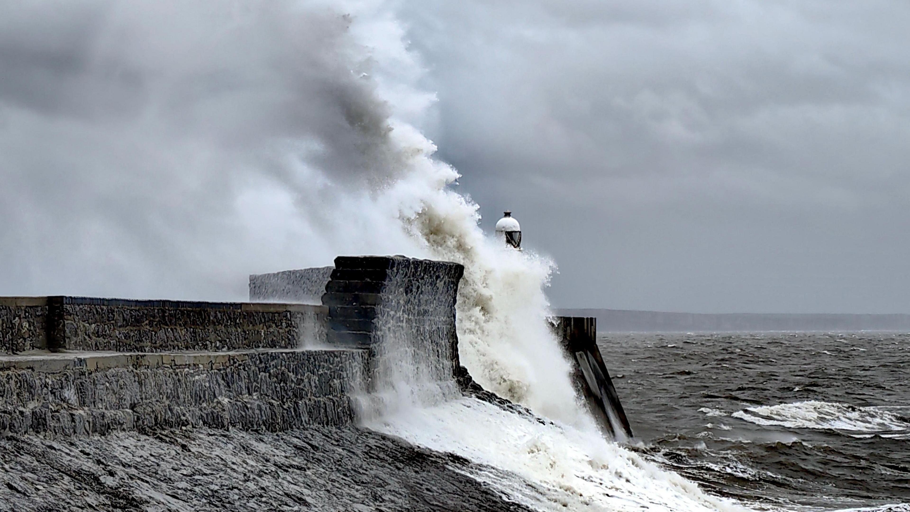 A wave crashes into a break wall in Wales