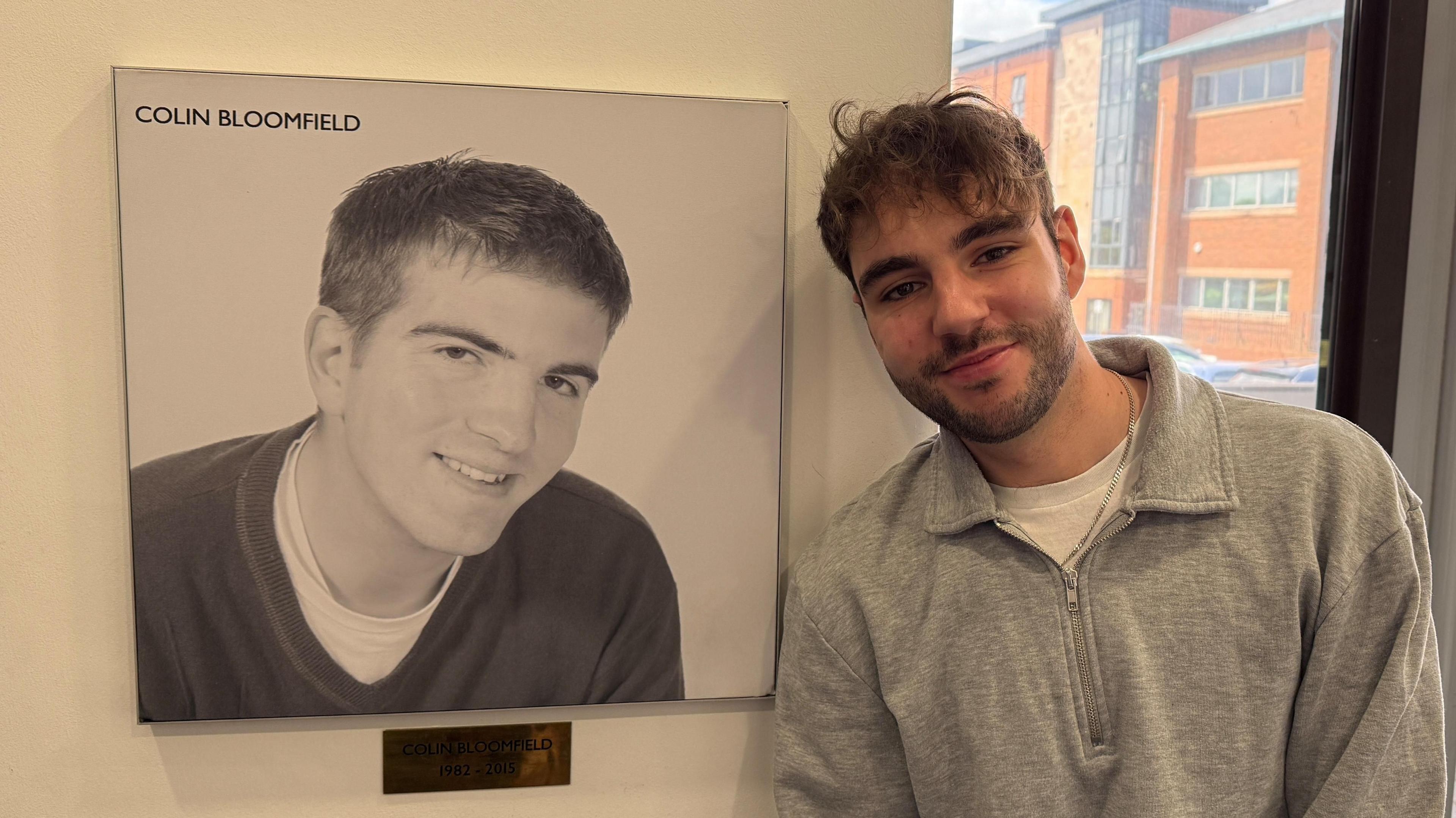 BBC Radio Derby producer Mitchell Barwell standing next to a photo of the late presenter Colin Bloomfield.