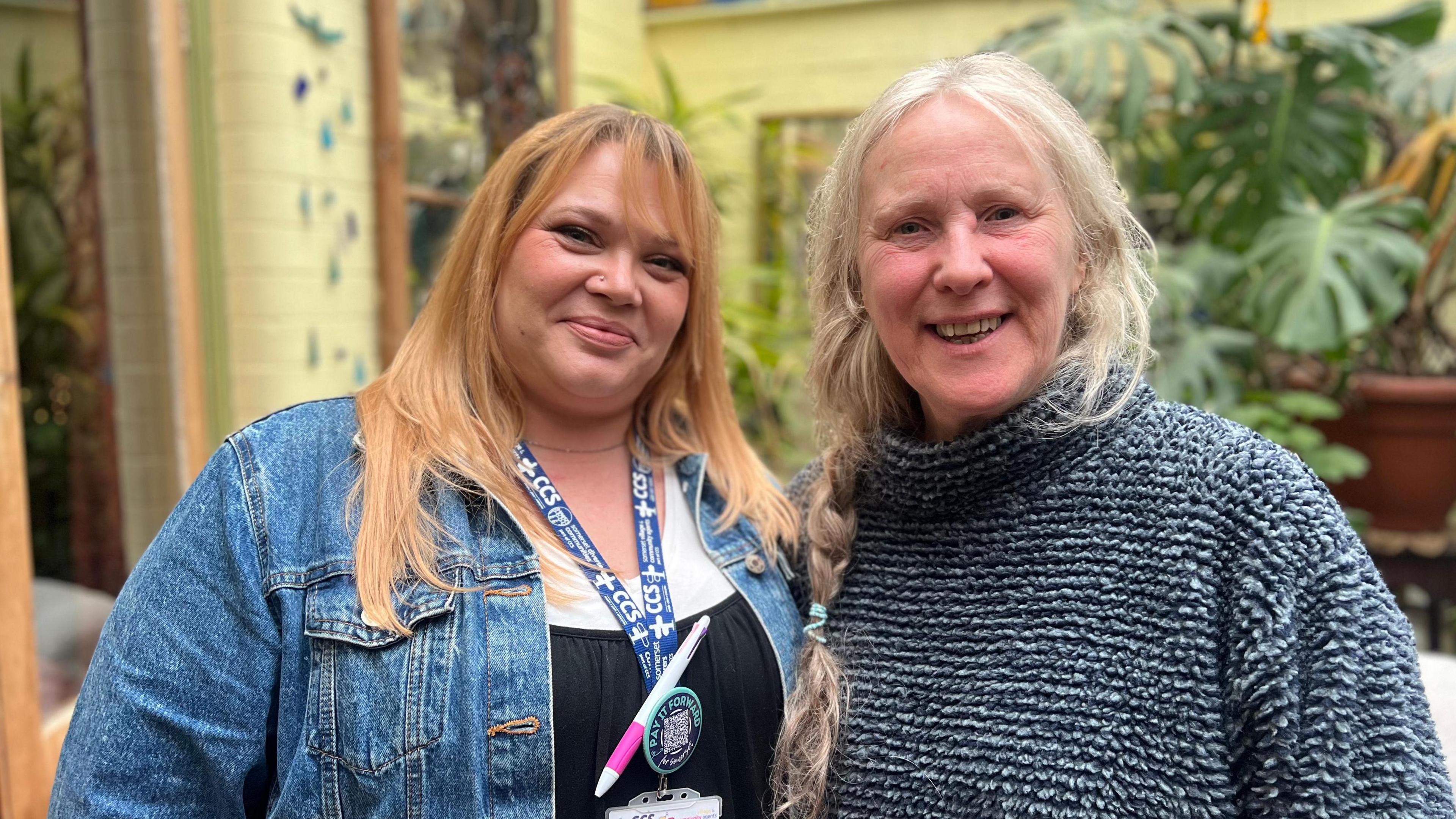 Two women smiling at the camera. One has ginger hair and is a blue jacket. The lady on the right is in a knitted jumper with grey hair.