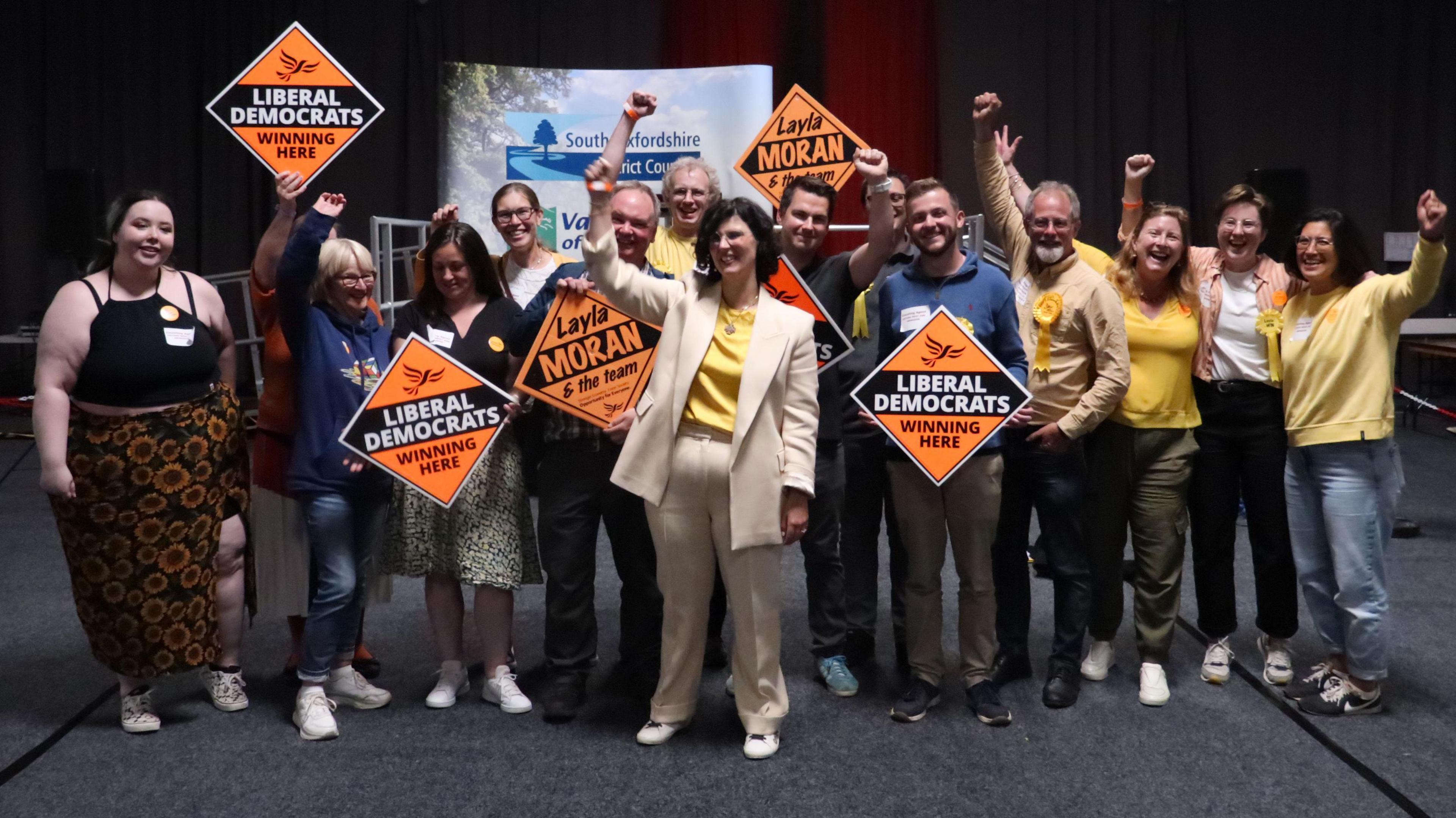 Layla Moran in a cream suit and white shoes, with about 12 supporters cheering 