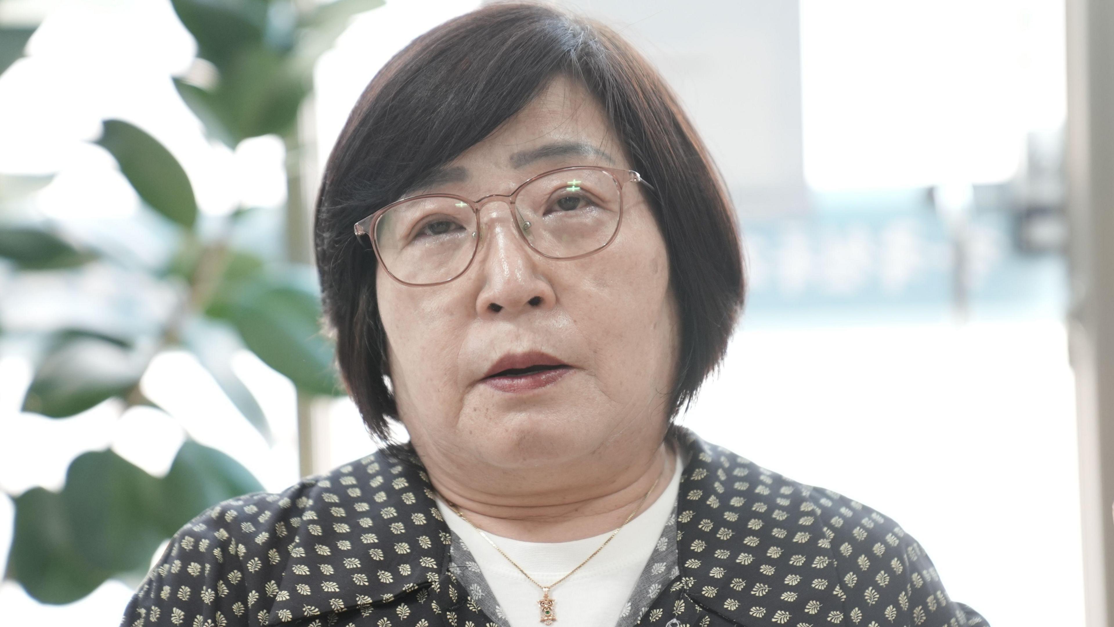 A middle-aged woman with short black hair and glasses looks into the camera