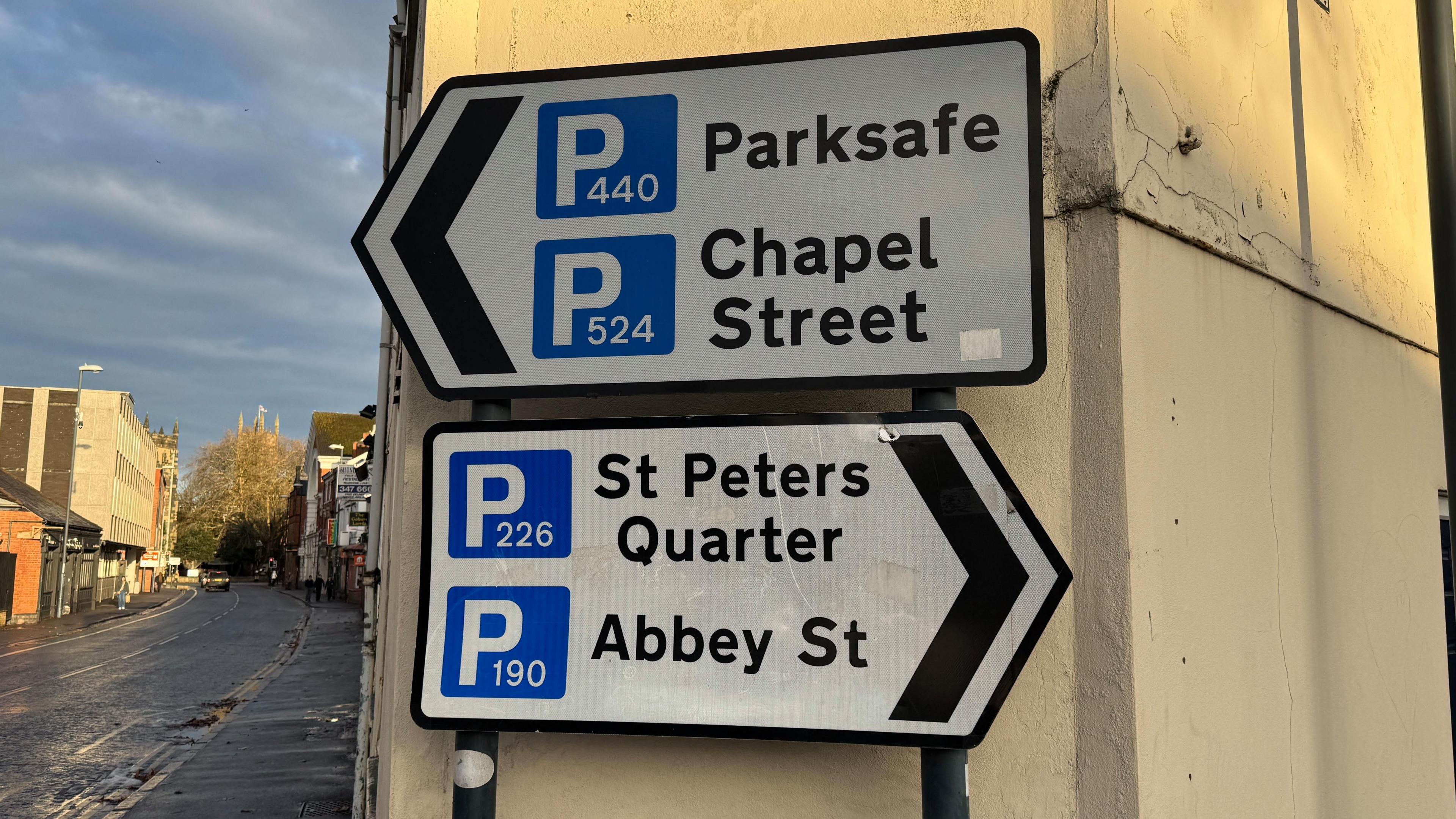 Two street signs mounted on a narrow corner building pointing to four different car parks - two in each direction.