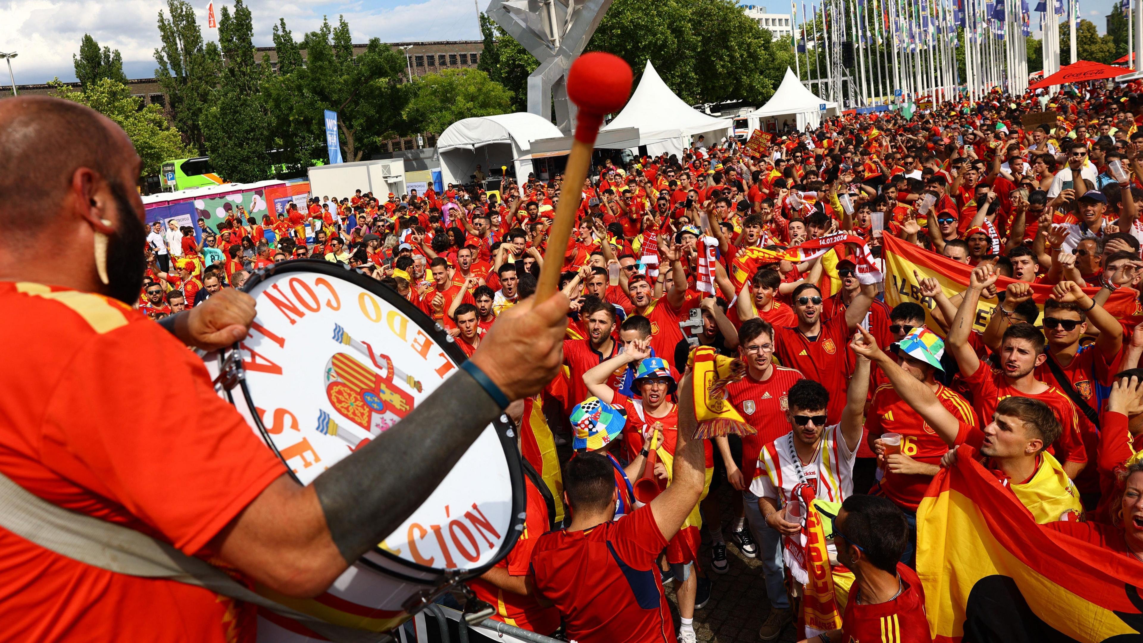 Spain fan plays a drum in front of a crowd of Spanish fans wearing red and yellow