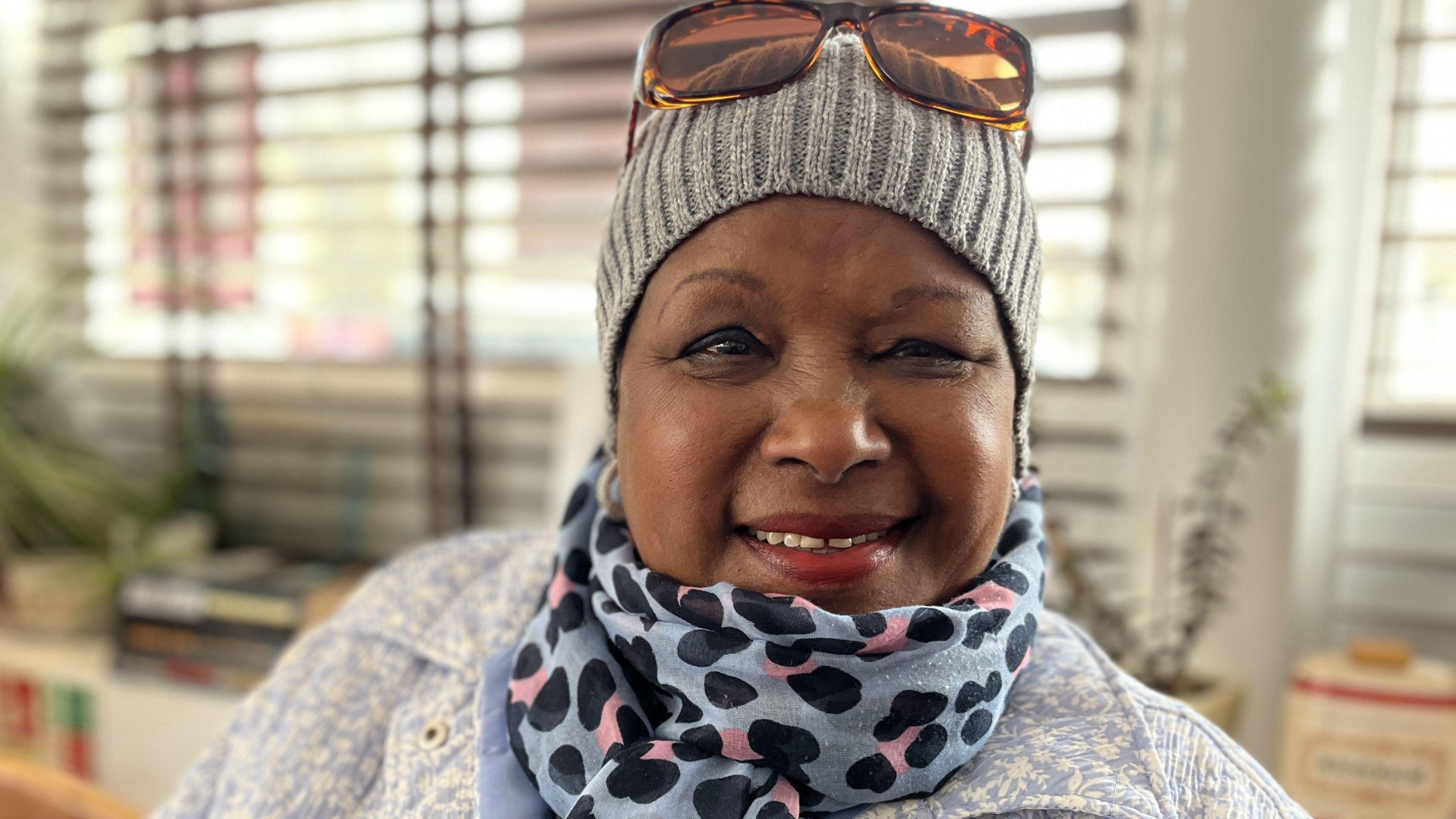 Cafe user, Rozza, smiling wearing a bobble hat, scalf and sun glasses on her head