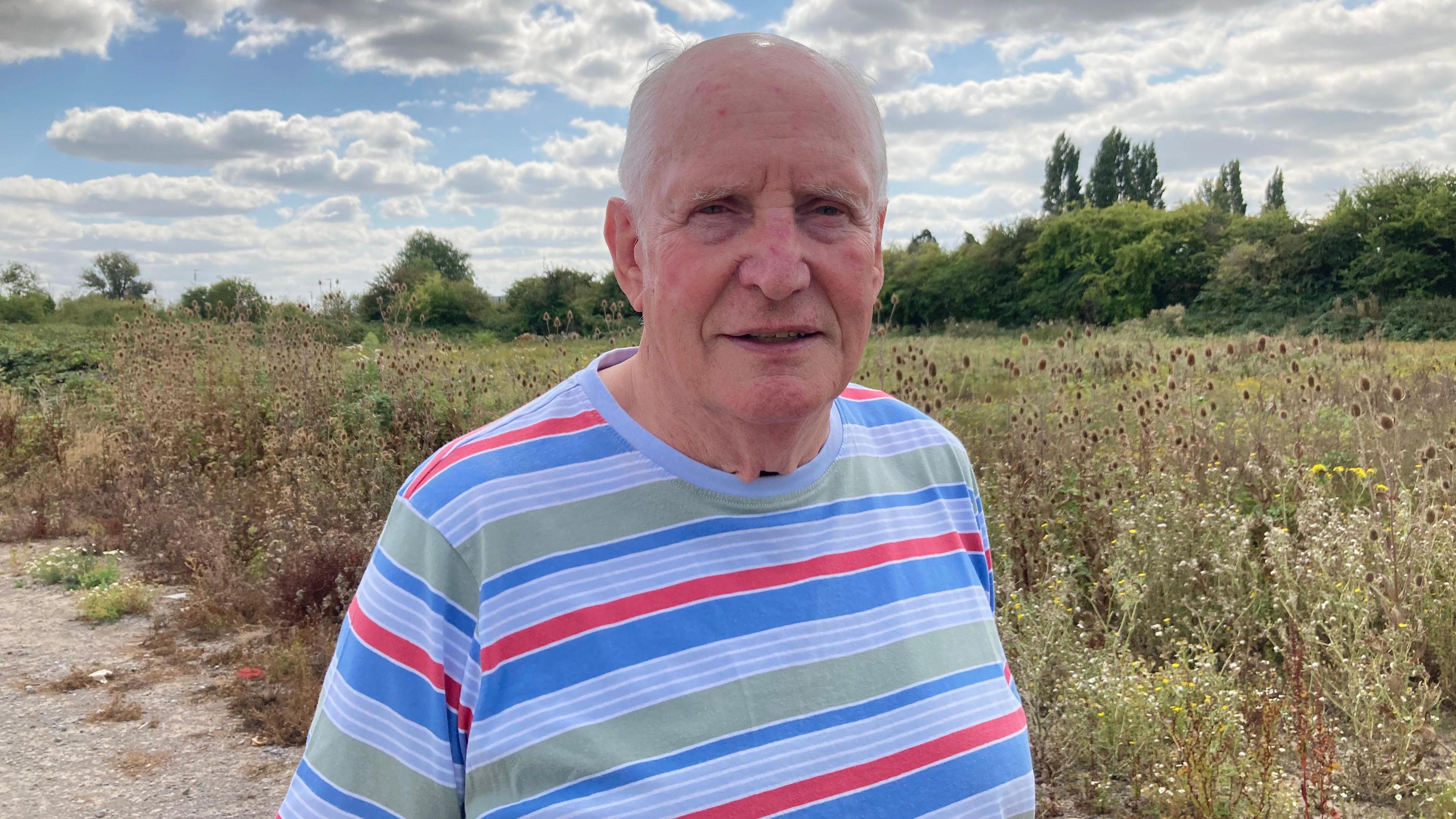A man in a striped shirt is standing next to a field. He is smiling at the camera.