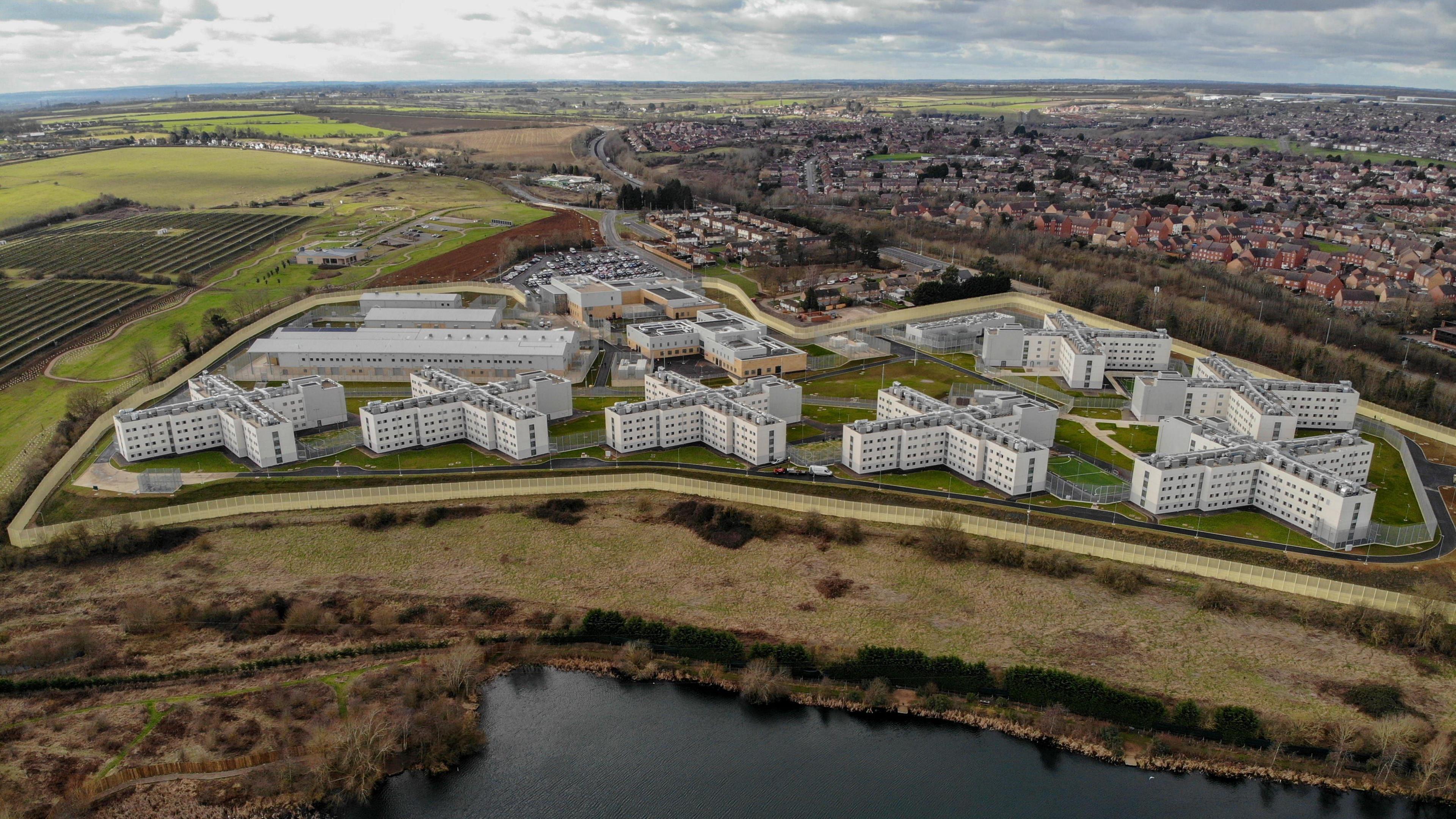 An aerial shot of HMP Five Wells showing the seven cross-shaped housing blocks with the town of Wellingborough in the background.