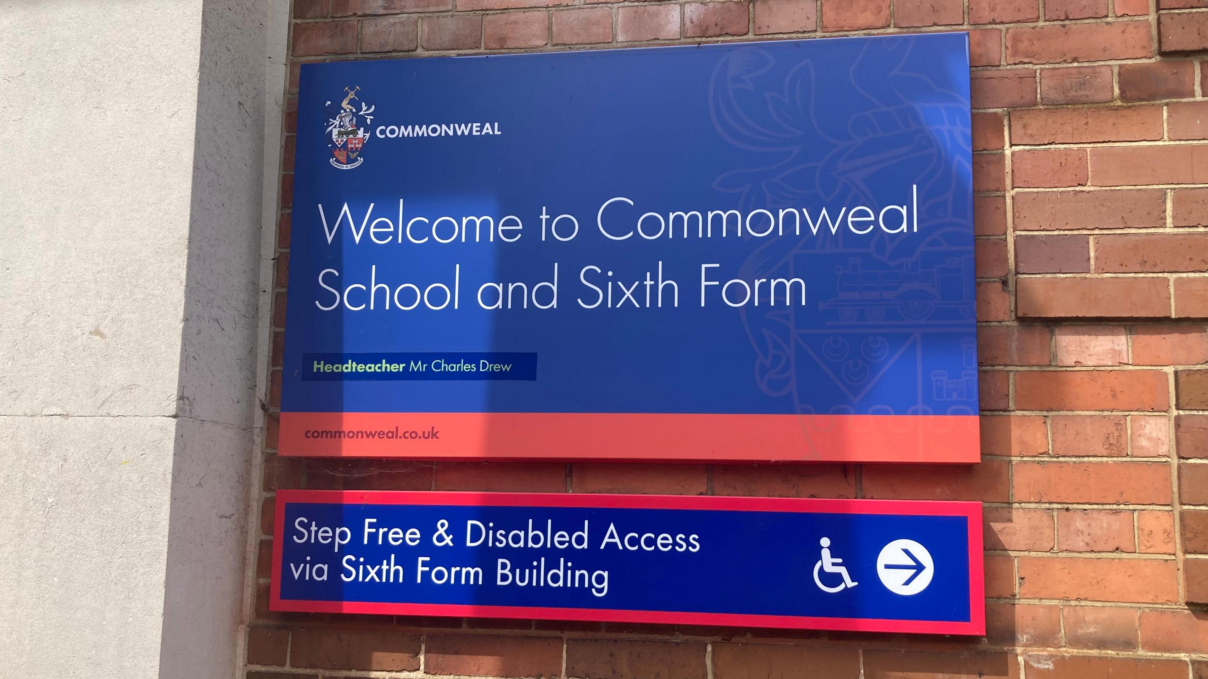 Red and blue sign for Commonweal School on a brick wall