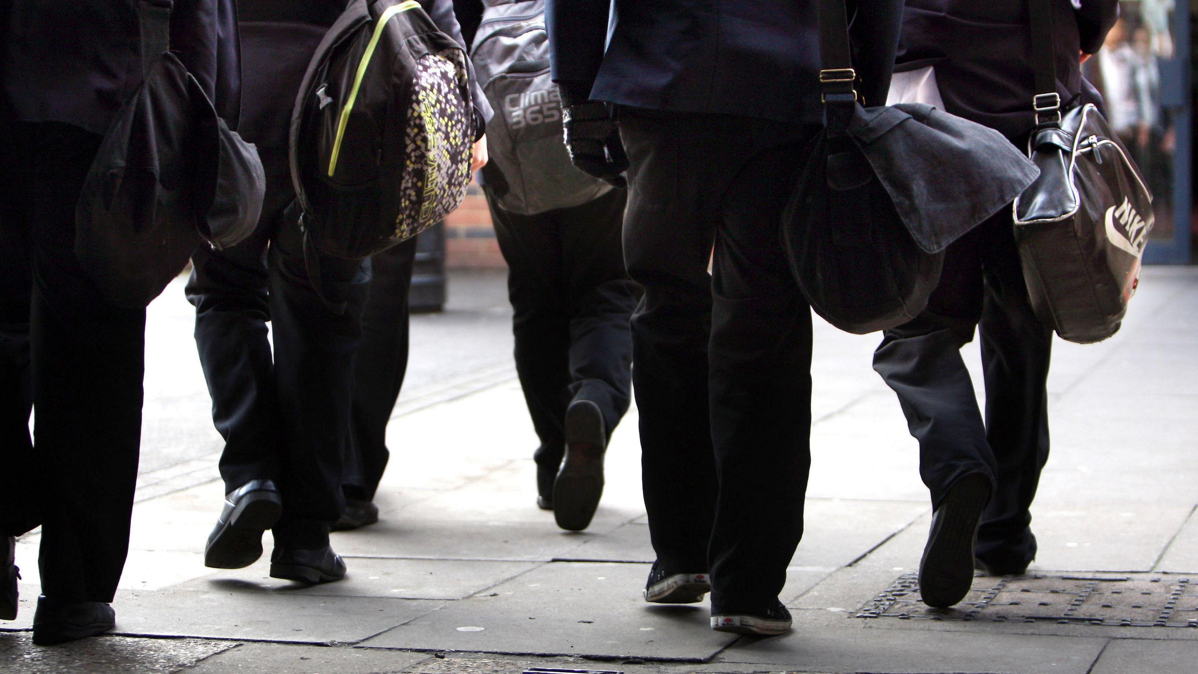 An image showing the backs of students trouser legs as they walk away from the camera. The students are carrying shoulder bags and rucksacks. 