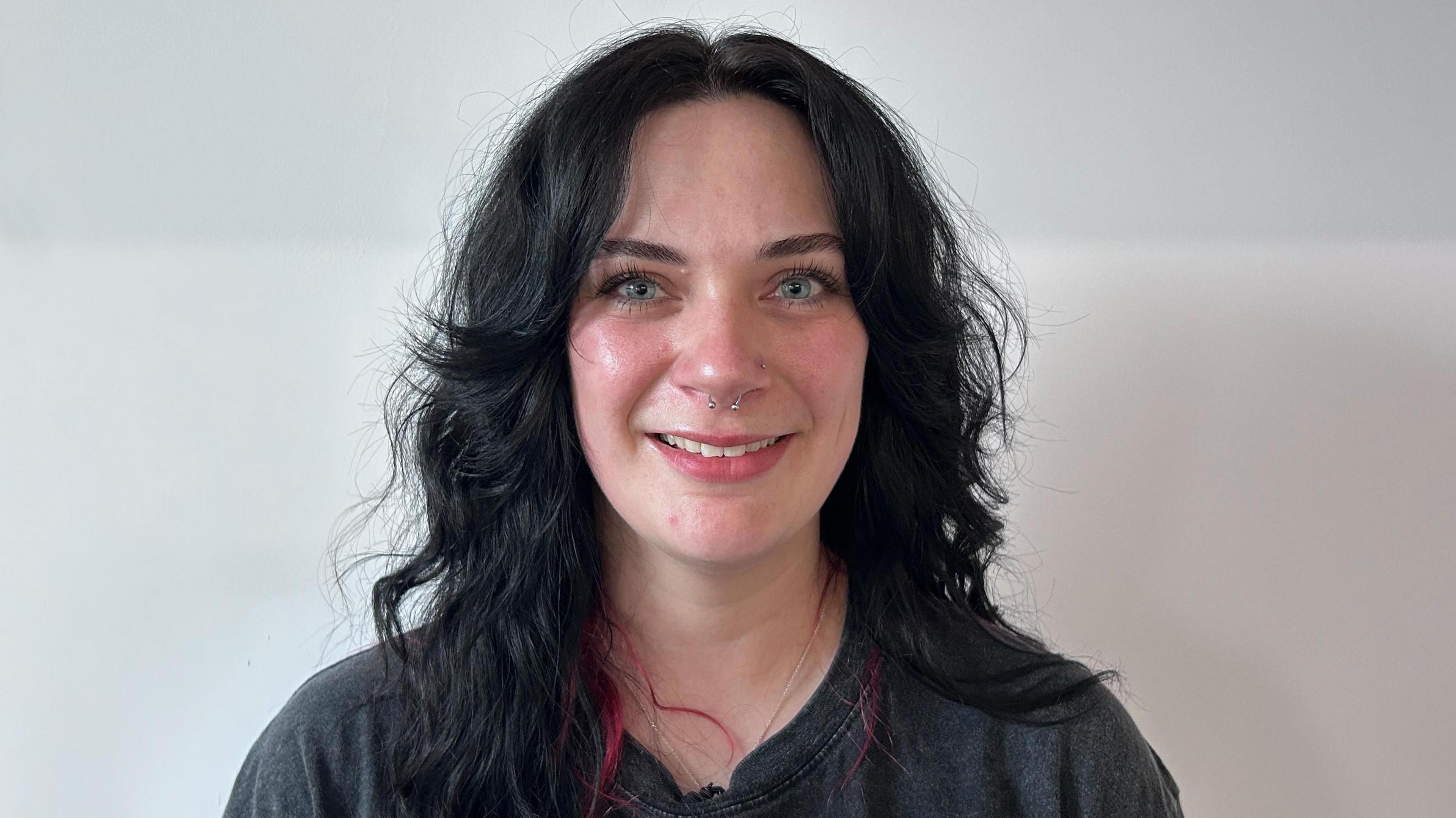 Abbey Parrinello, who has black hair with red tips and blue eyes. She has a septum piercing and is smiling in the photo.