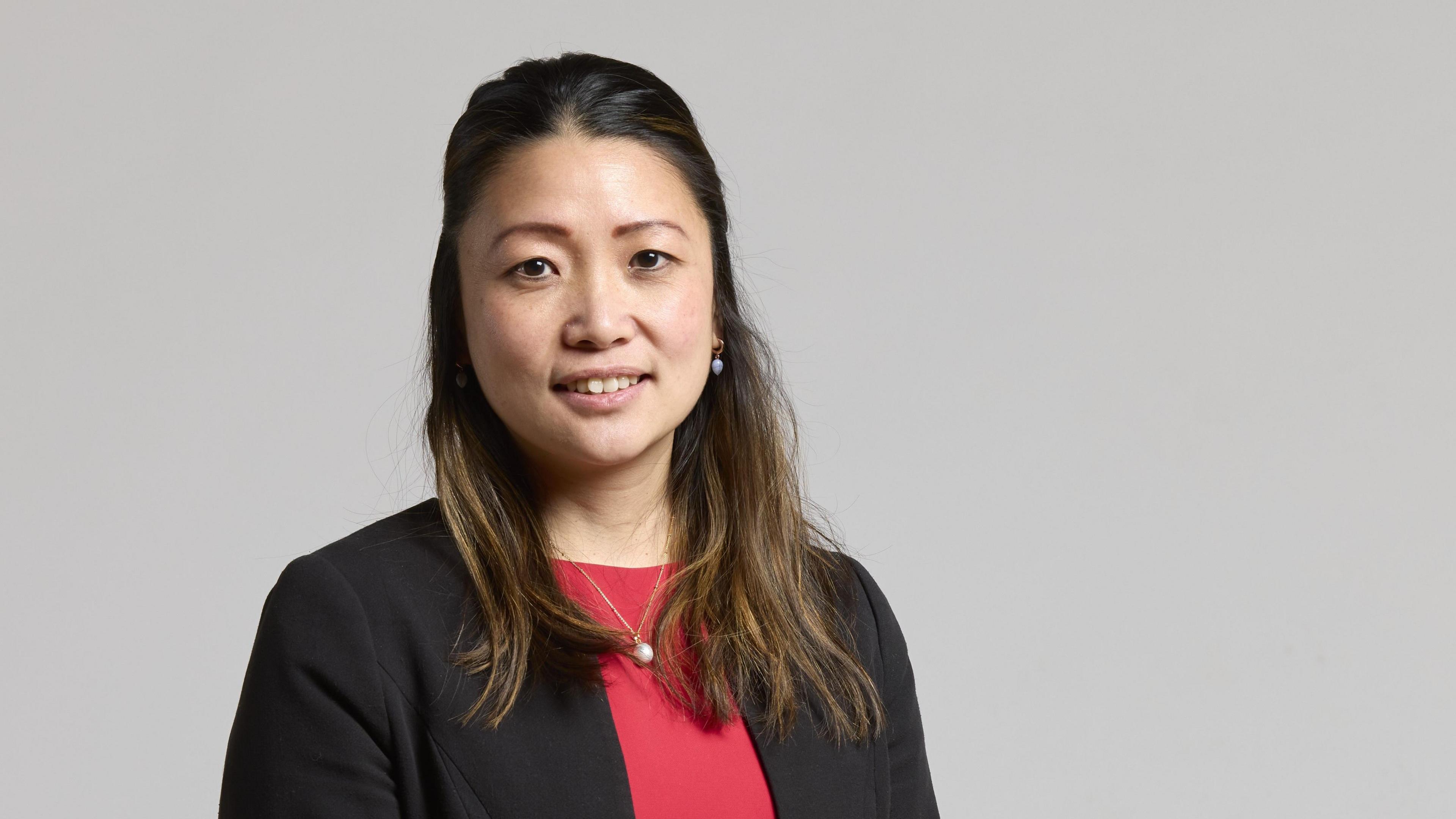 A woman in a red top and black blazer smiles at the camera. 