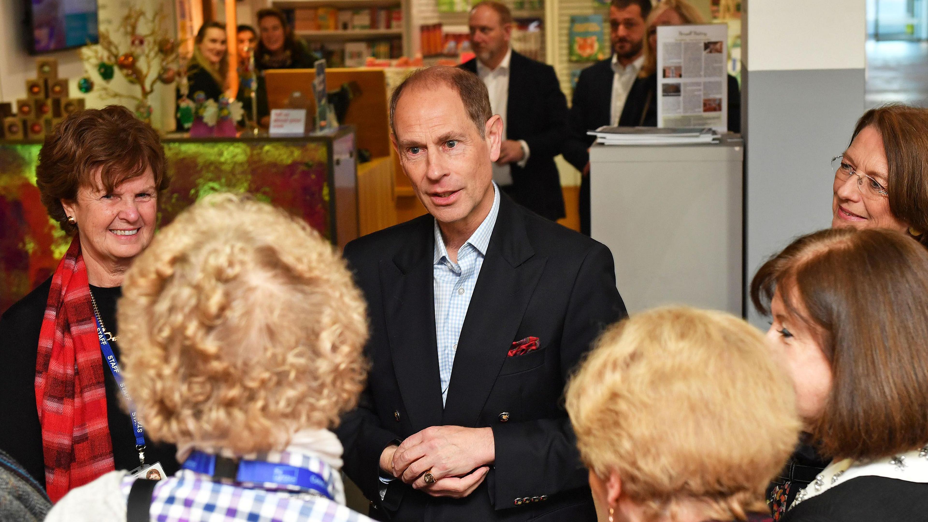 The Duke of Edinburgh wearing a blue suit jacket and pale blue shirt. He is stood talking to a person facing away from the camera. There a five women standing around him talking to him