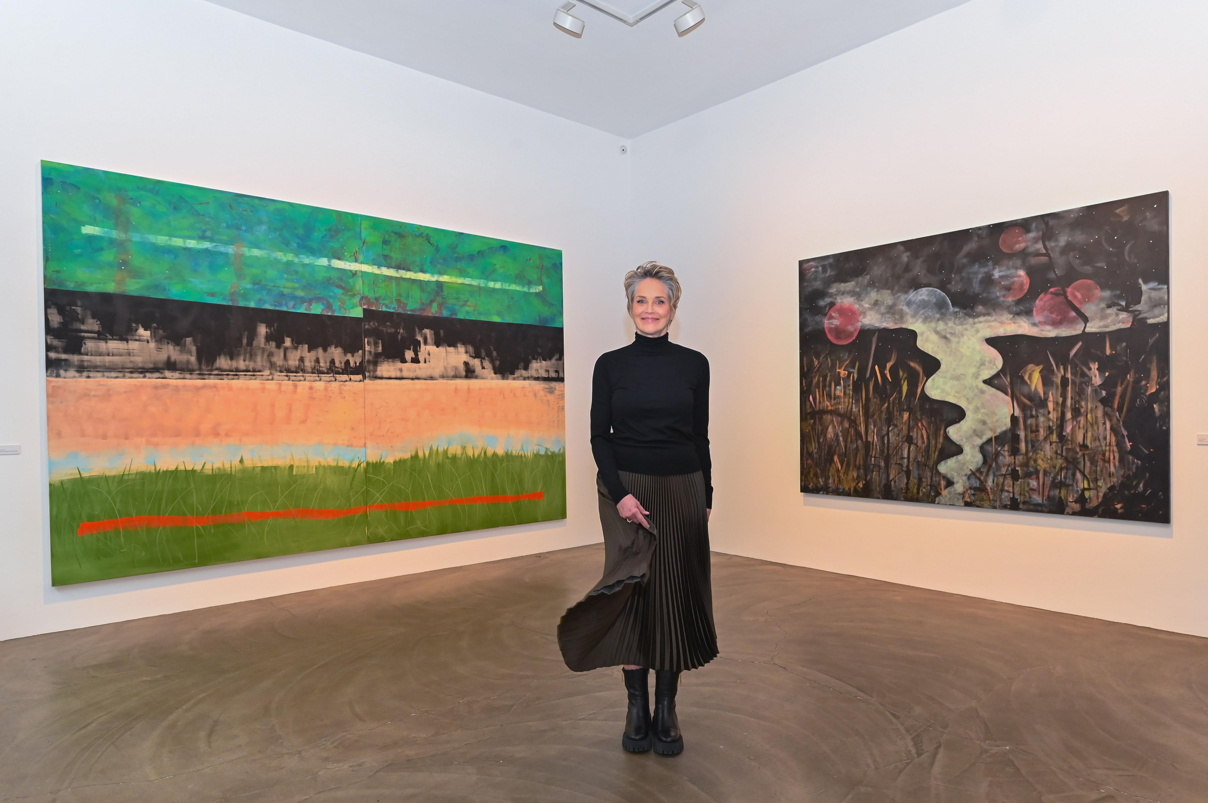 Sharon Stone in Berlin in a black sweater and pleated skirt in front of two large paintings