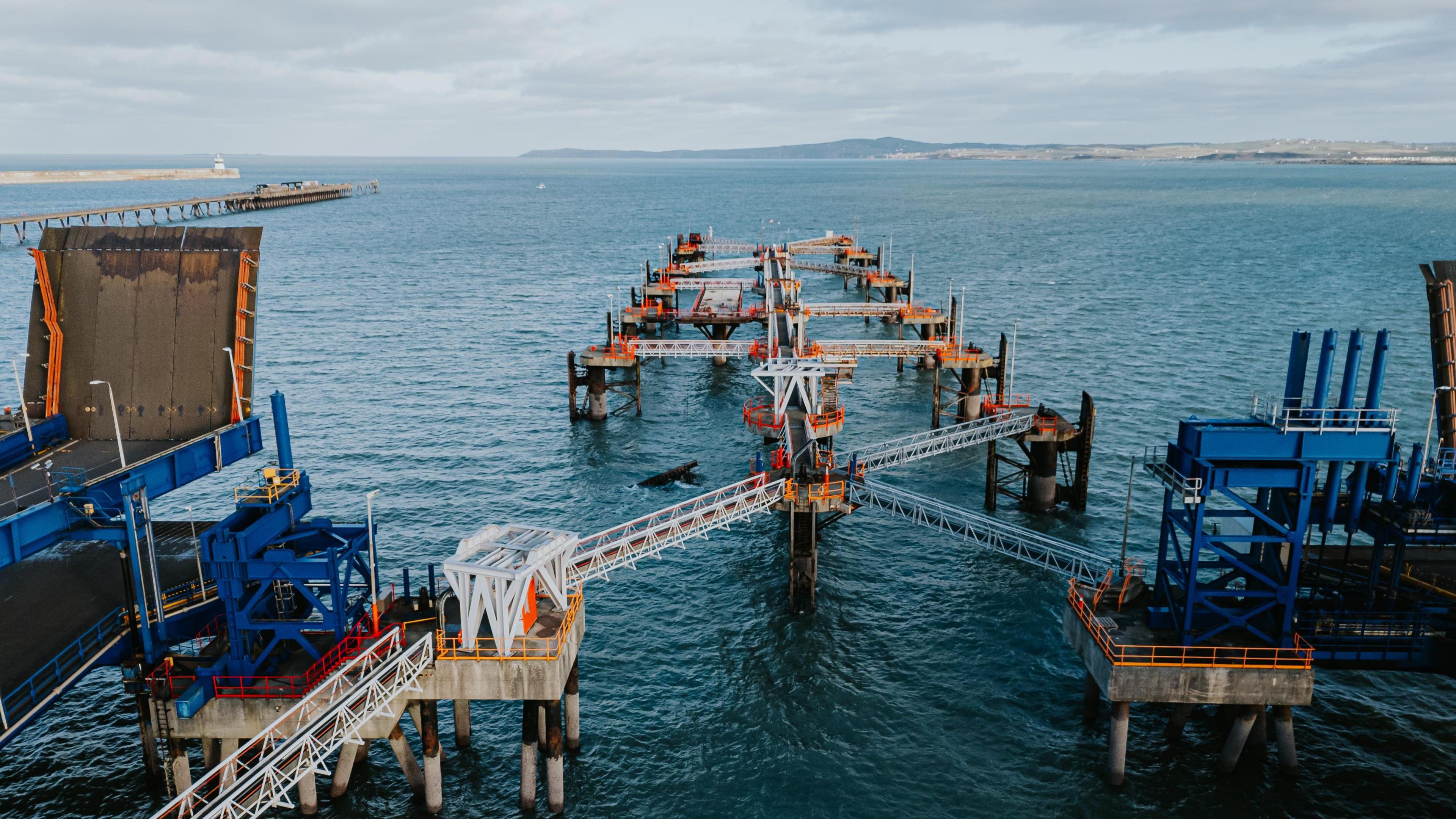 Holyhead port walkways jutting out of the sea. There is an object jutting out  of the sea which seems to have broken off of the port. 