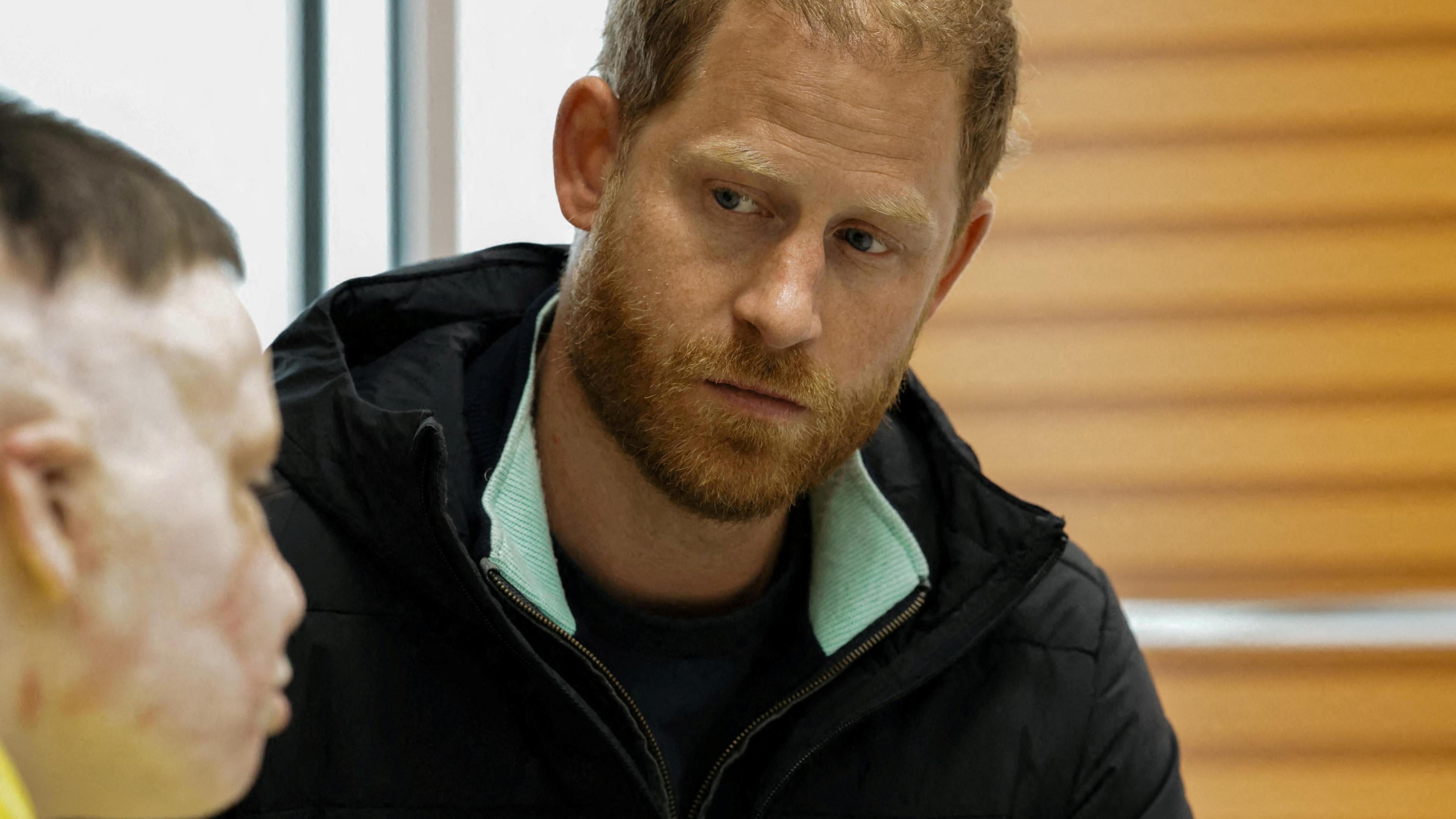 An image of Prince Harry, wearing a black jacket, speaking to a wounded Ukraine war veteran.