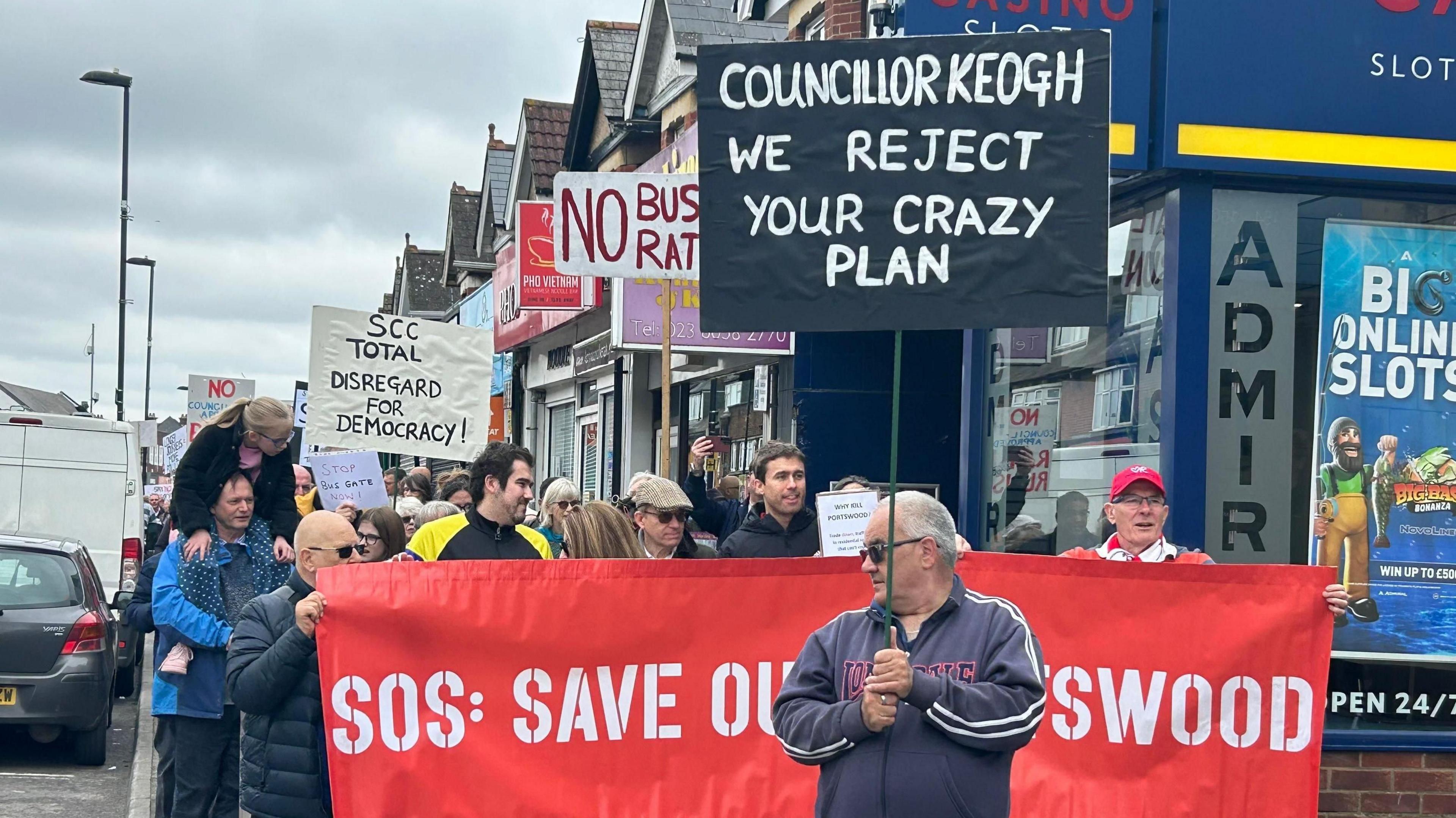 A group of people walking down the street holding placards and signs opposing the Portswood bus gate scheme.