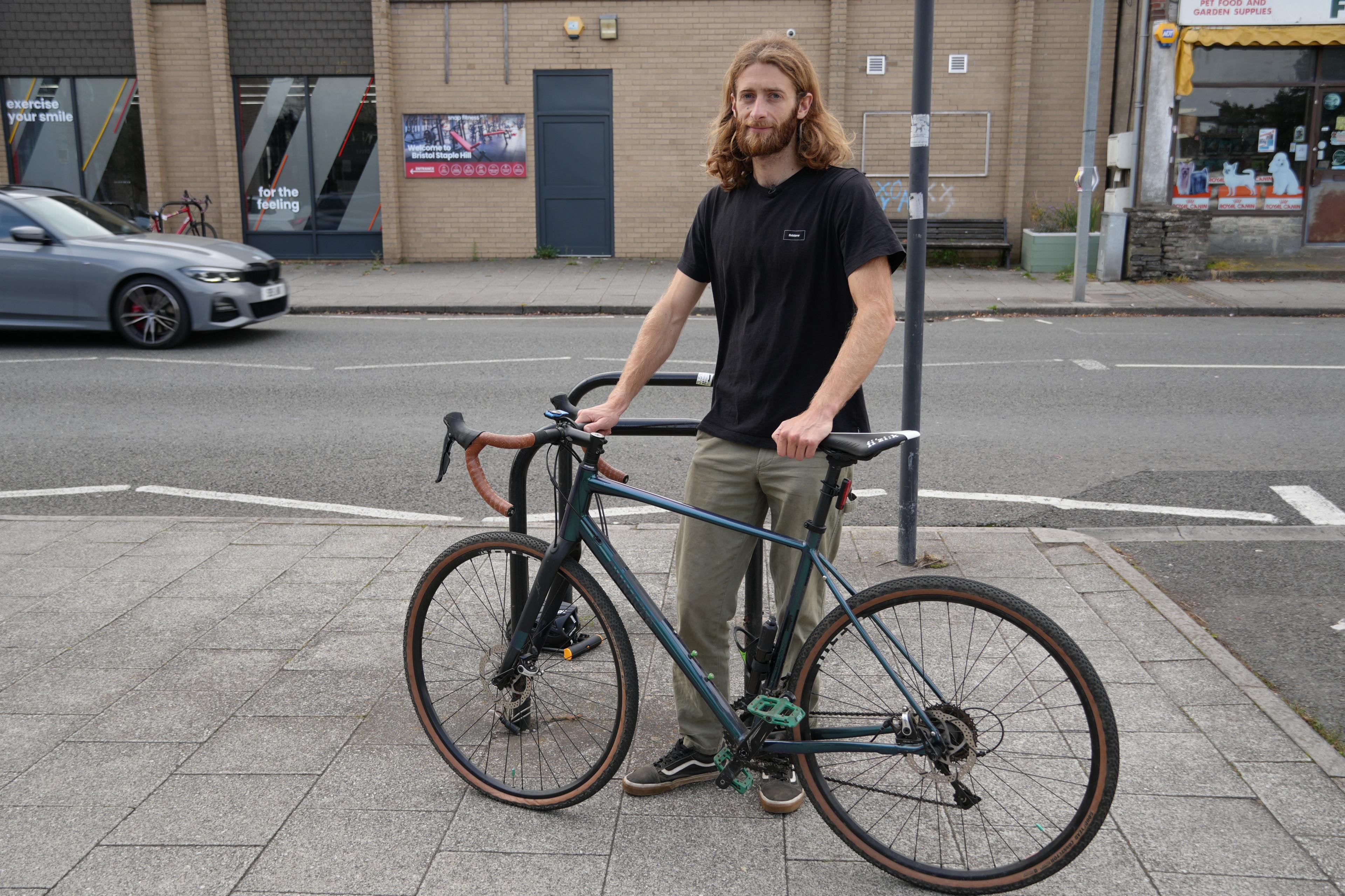 Josh is standing on the pavement holding his bike 