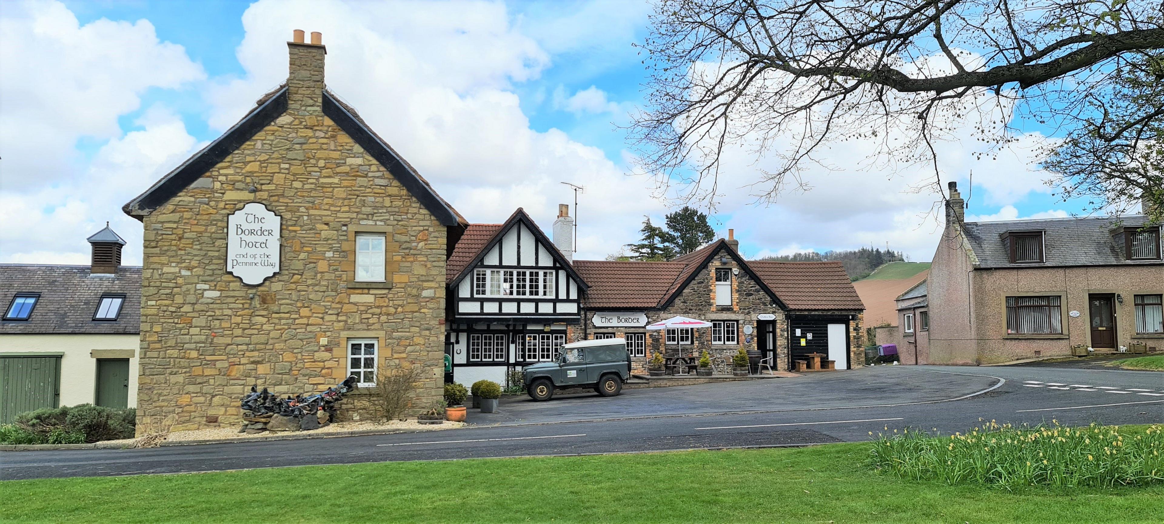 An old hotel building in the Borders next to a road with grass and daffodils growing in front of it