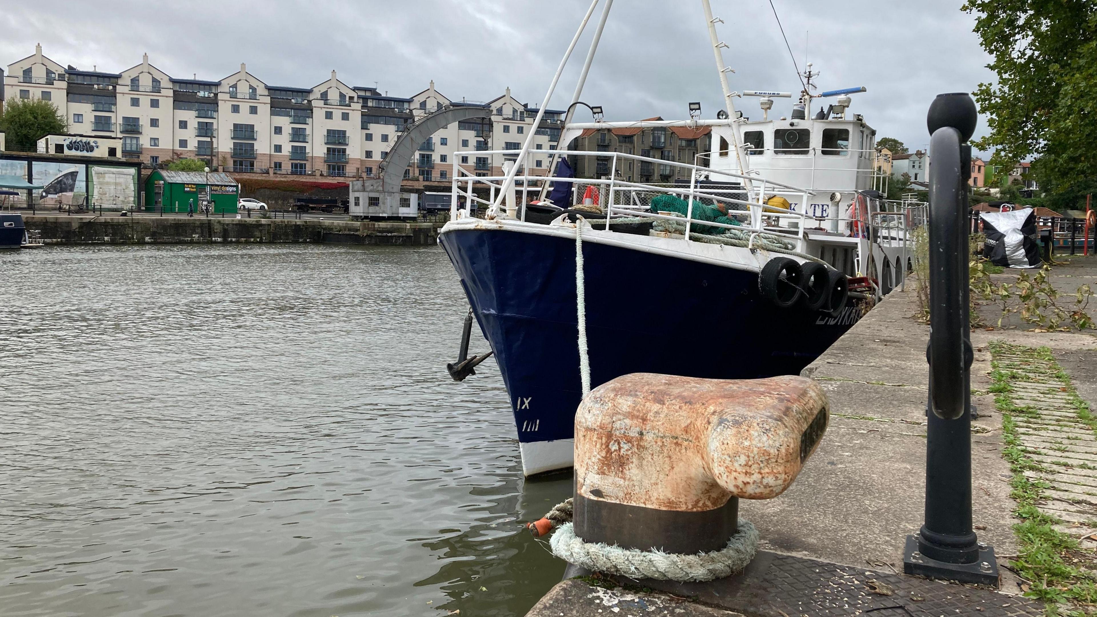 A wide view of the Lady Kate boat with the mooring line in the foreground. The Bristol harbour waters can be seen on the left with a few harbourside apartments in view in the background.