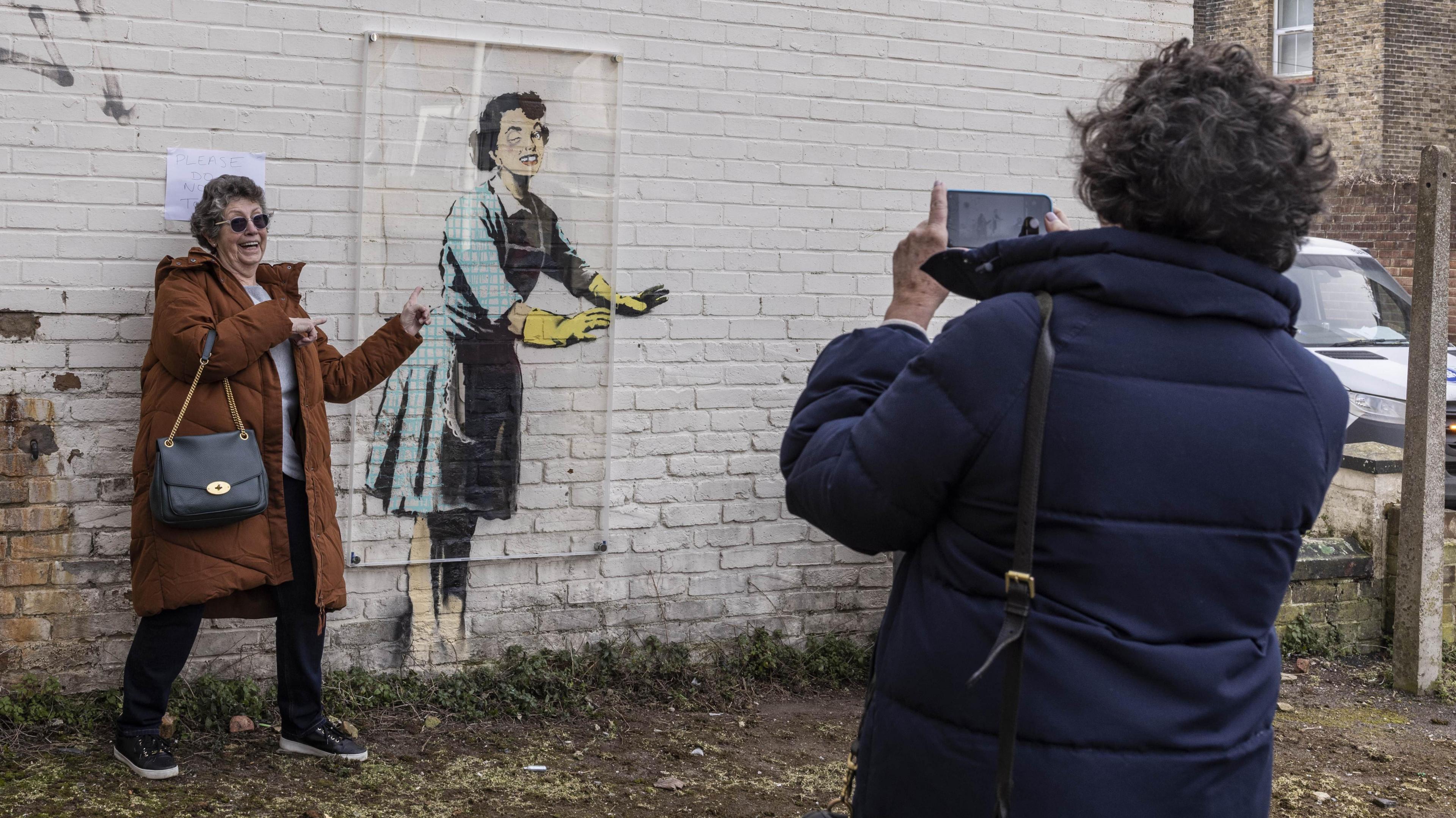 A woman in a brown coat having her picture taken next to the artwork after the freezer was removed.