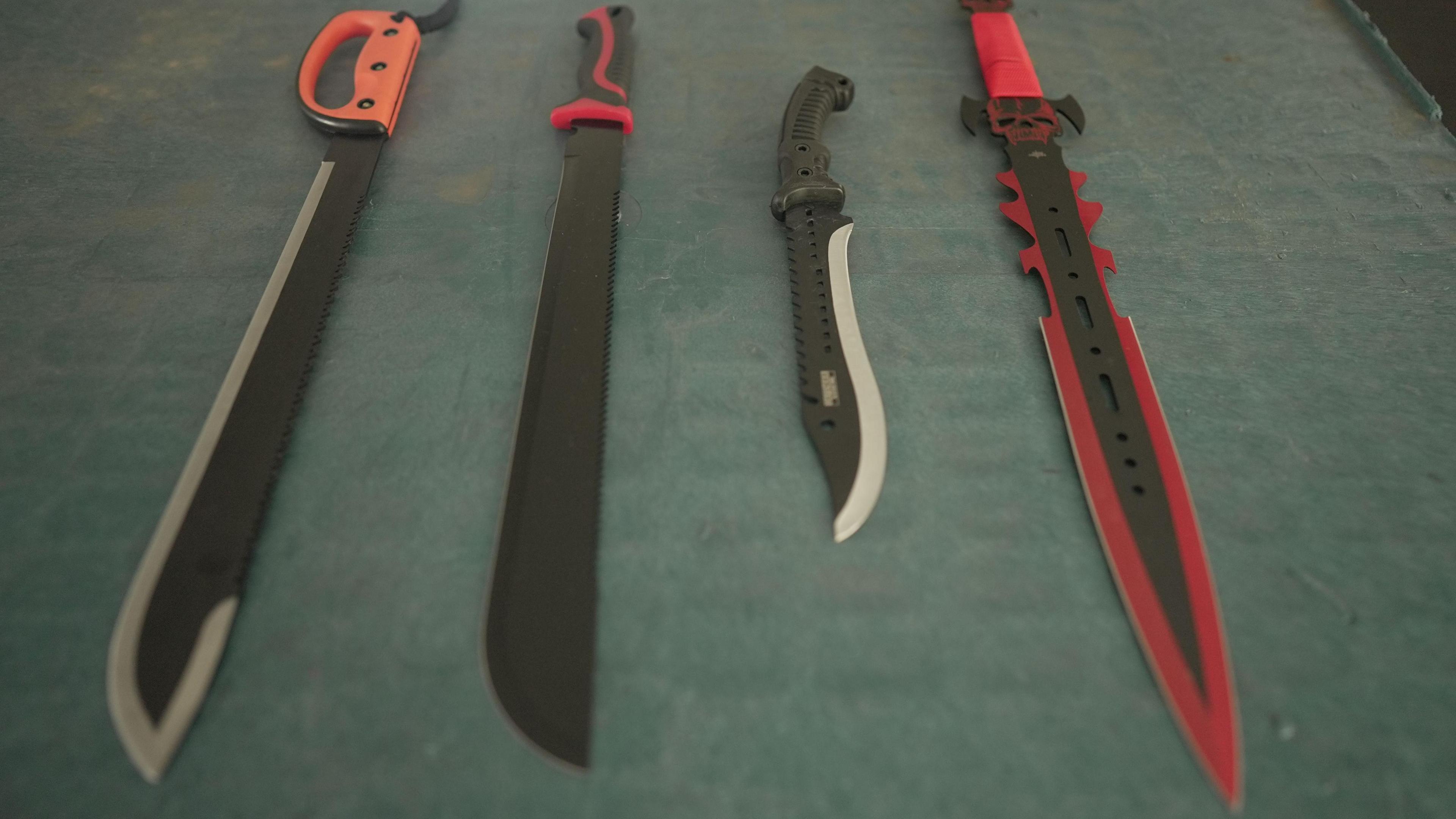 Four knives lying on a table in a row. They are varying in length but are all zombie knives