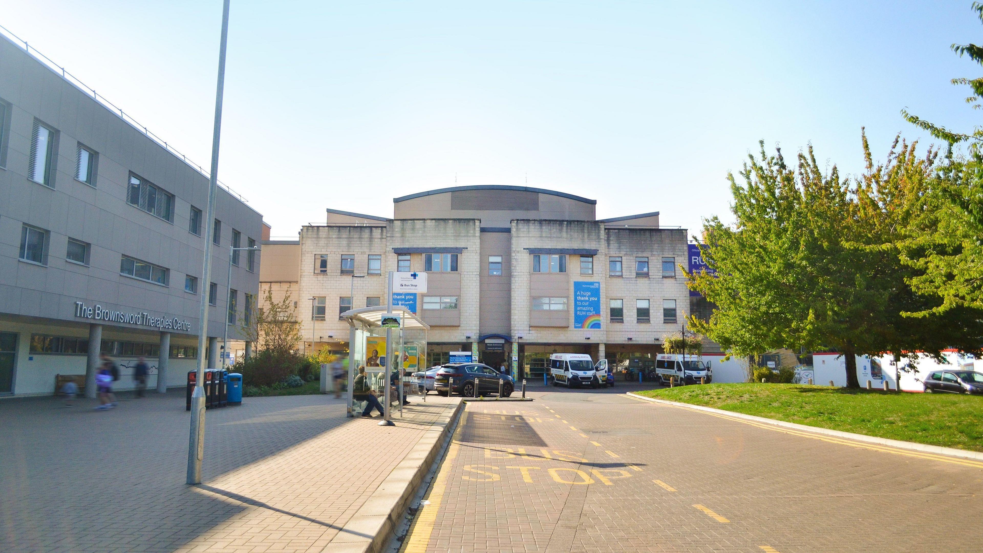 The road leading up to the entrance of RUH with a few vehicles outside and a person waiting at a bus stop