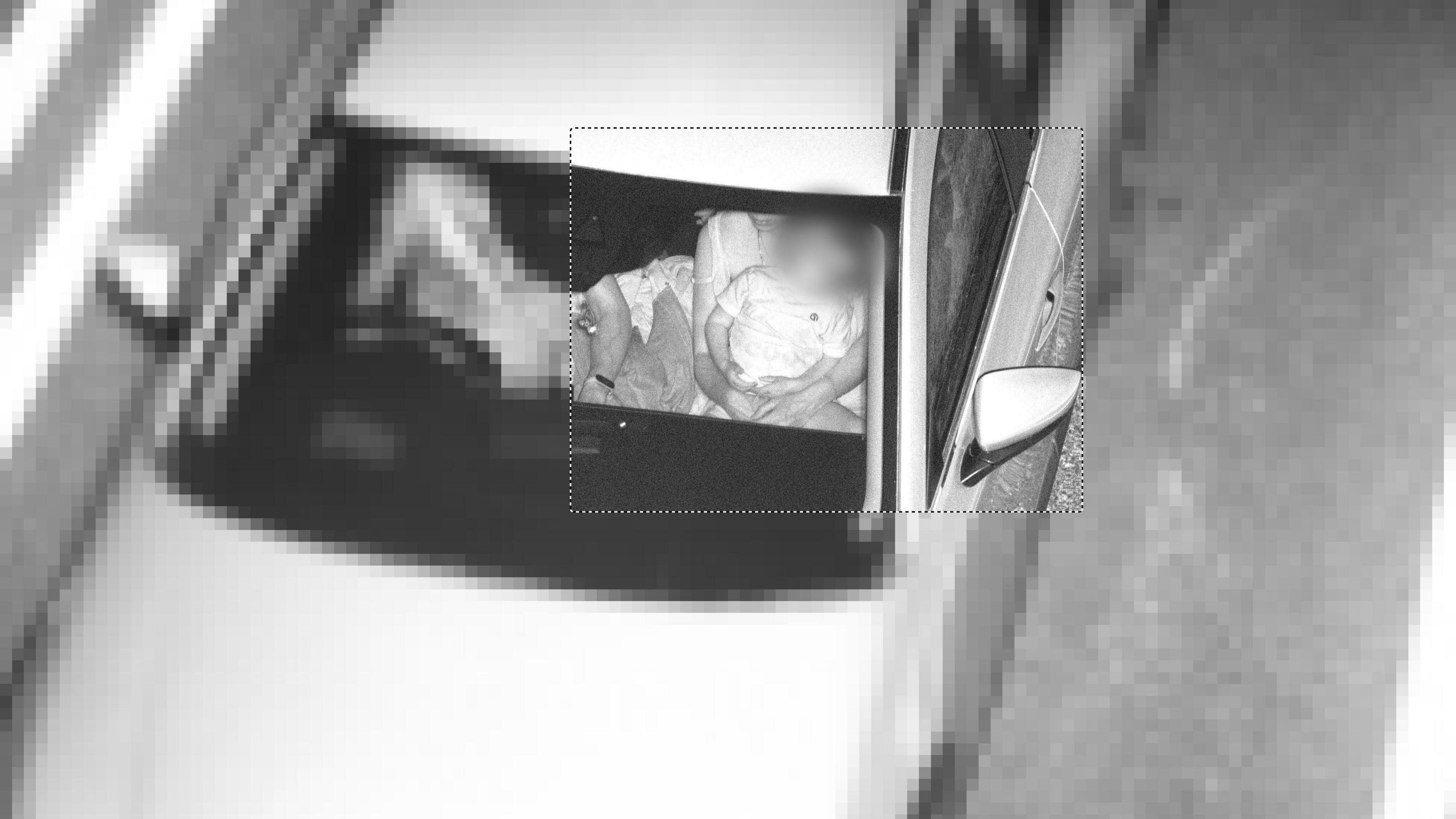 A black and white image taken from above, showing a child sitting unrestrained on a woman's lap in the front passenger seat.