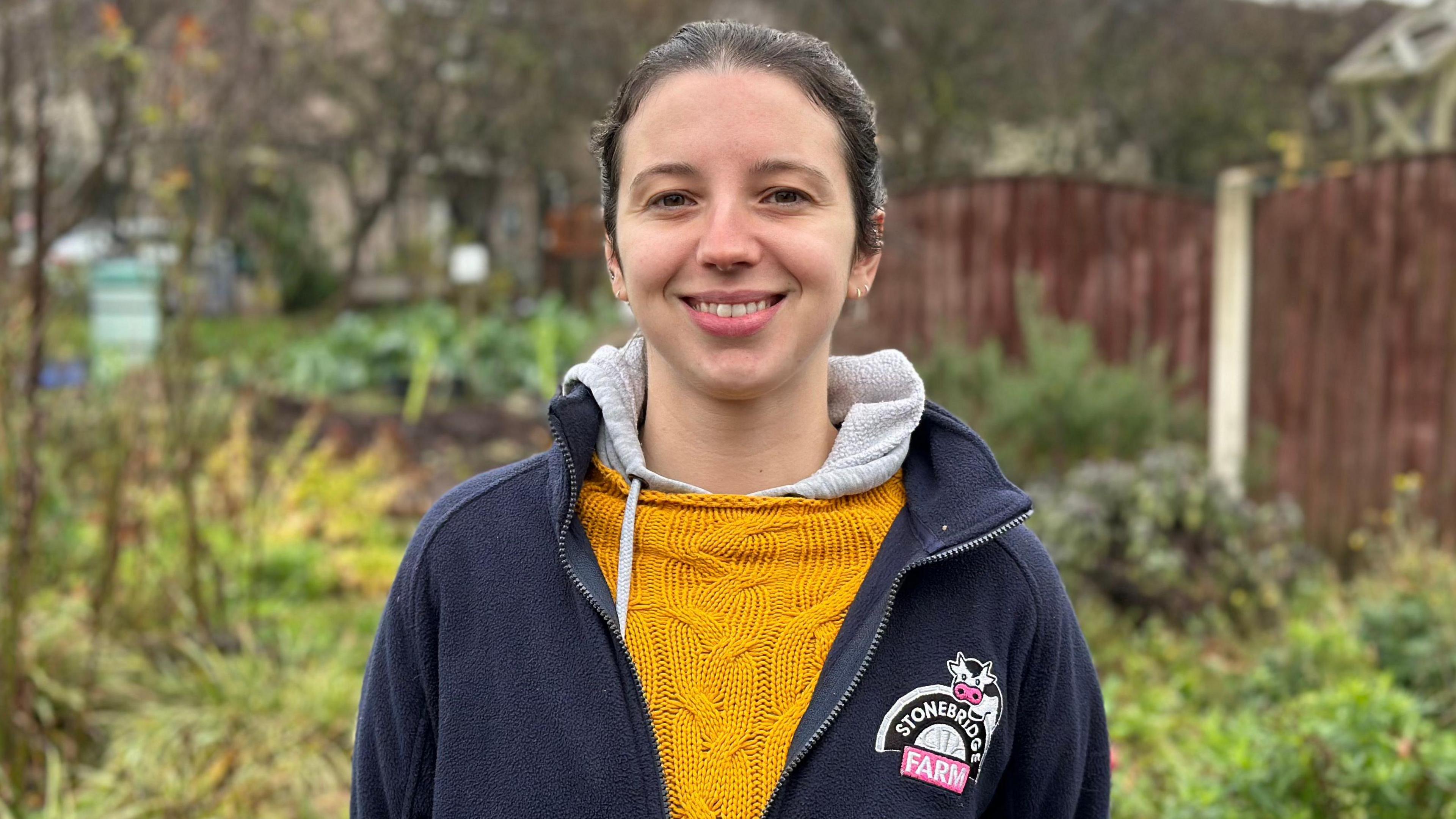 Grace Devey is pictured smiling at the camera. She is wearing a jumper with the Stonebridge City Farm logo