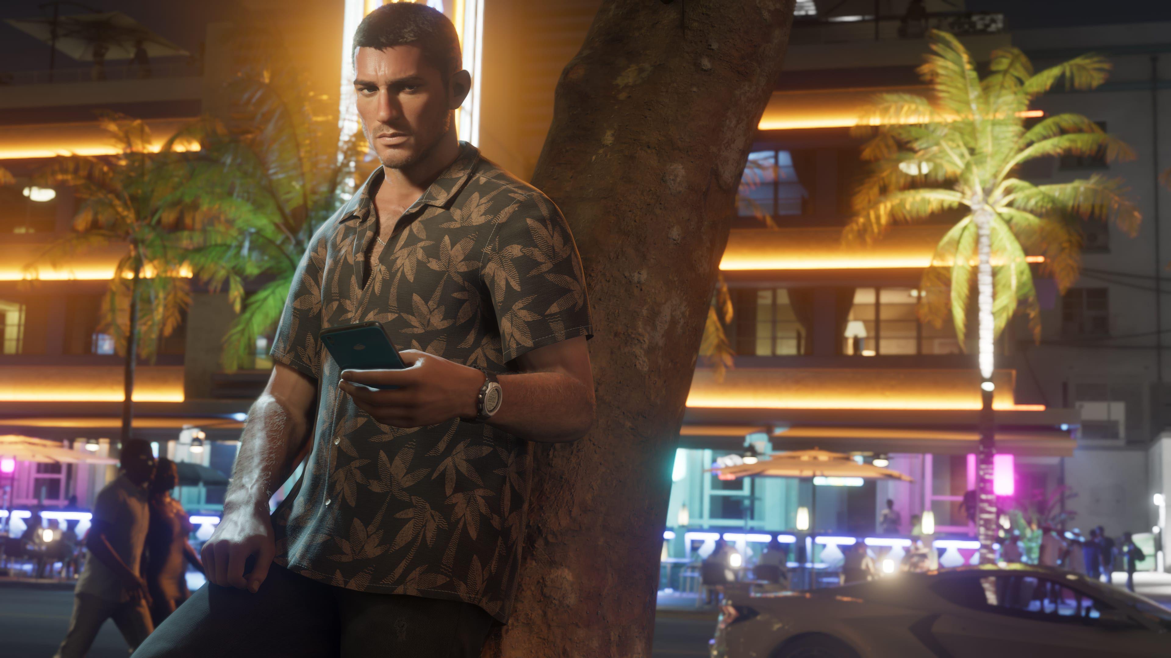 GTA 6 protagonist Jason Duval lean against a tree in a screenshot from the game, with buildings and cars on the strip behind him lit-up in blue, purple and yellow.