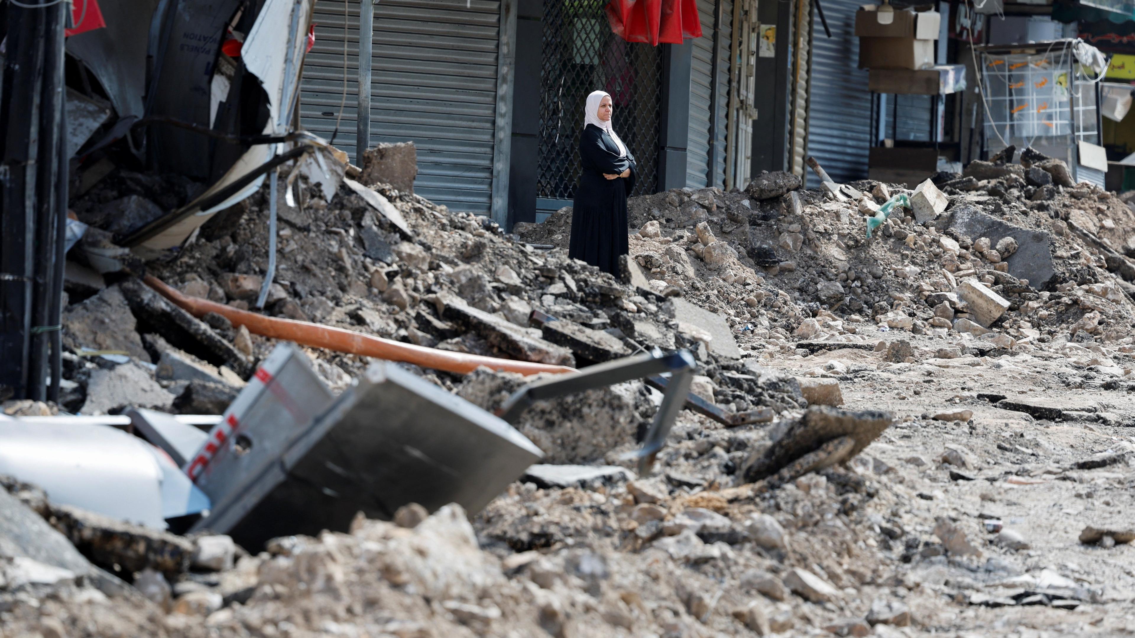 A Palestinian woman stands surrounded by rubble on a street in Jenin 