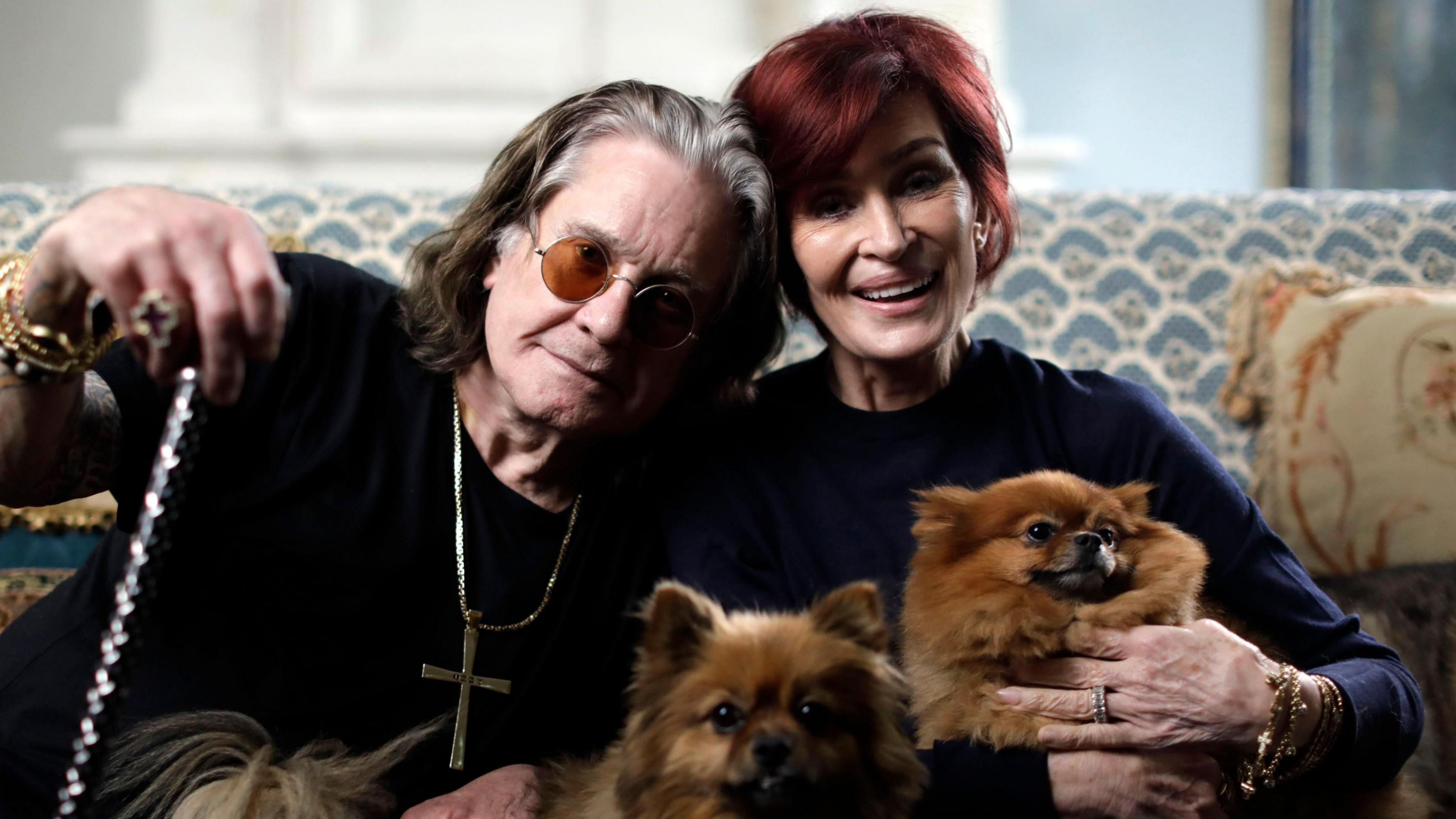 Ozzy and Sharon Osbourne sitting togehter on a sofa with two small dogs