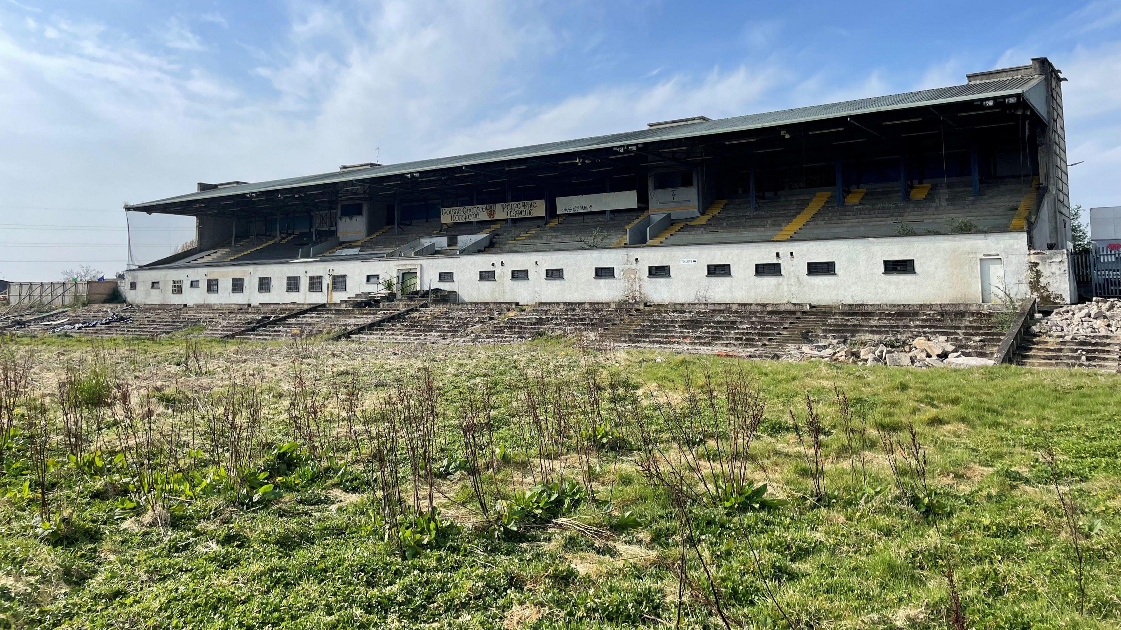 A run down stadium. Overgrown grass is in the foreground.