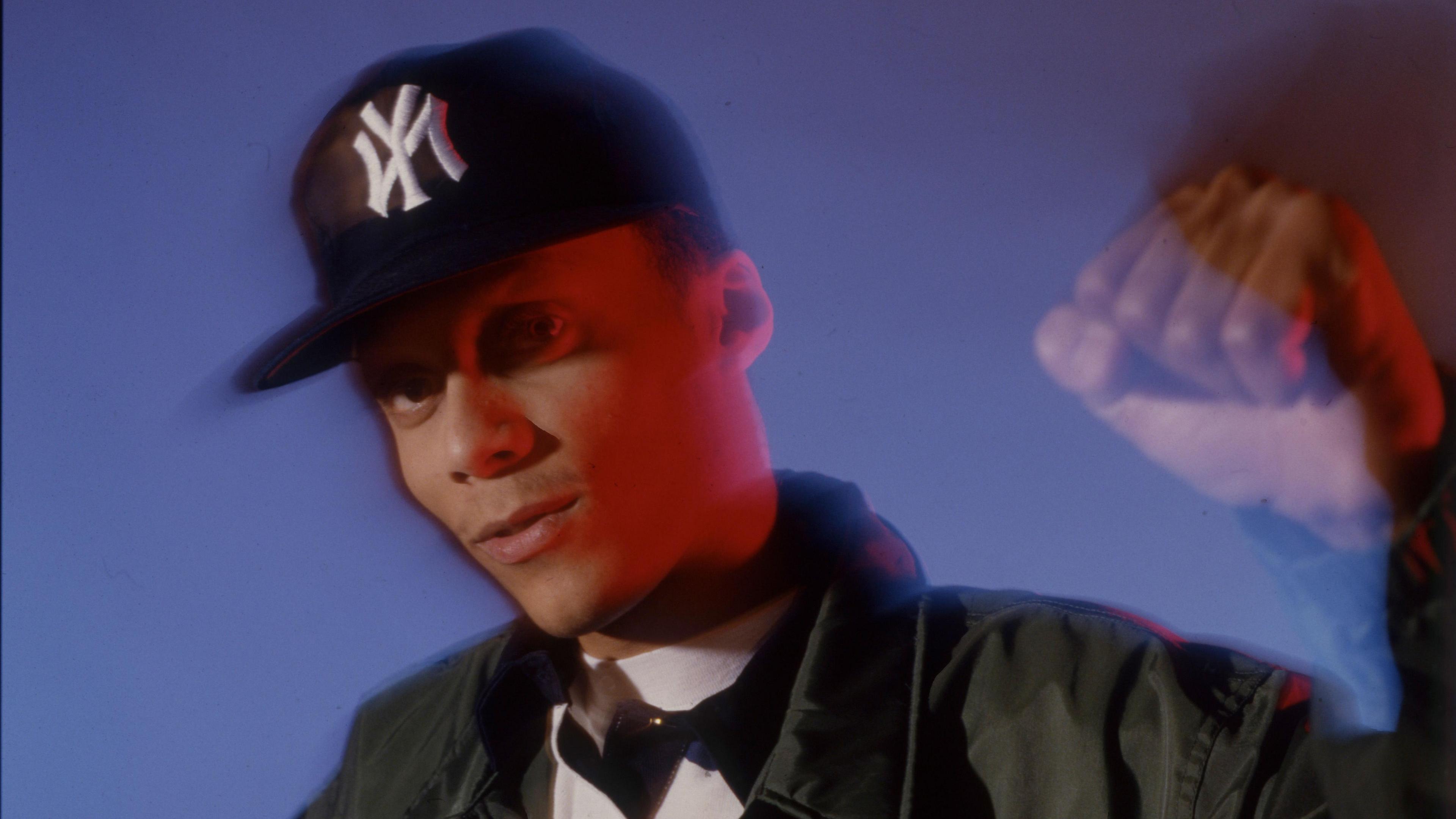 A young rapper wearing a black cap, raising his fist in the air.