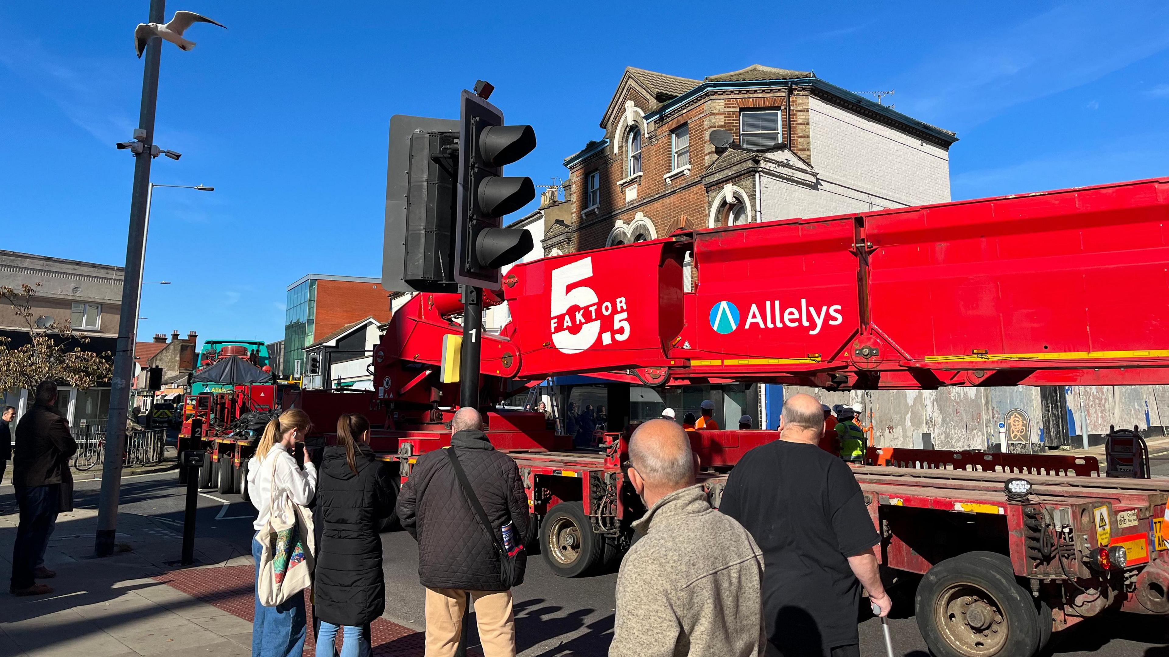 A large red vehicle passing through Ipswich as bystanders look on