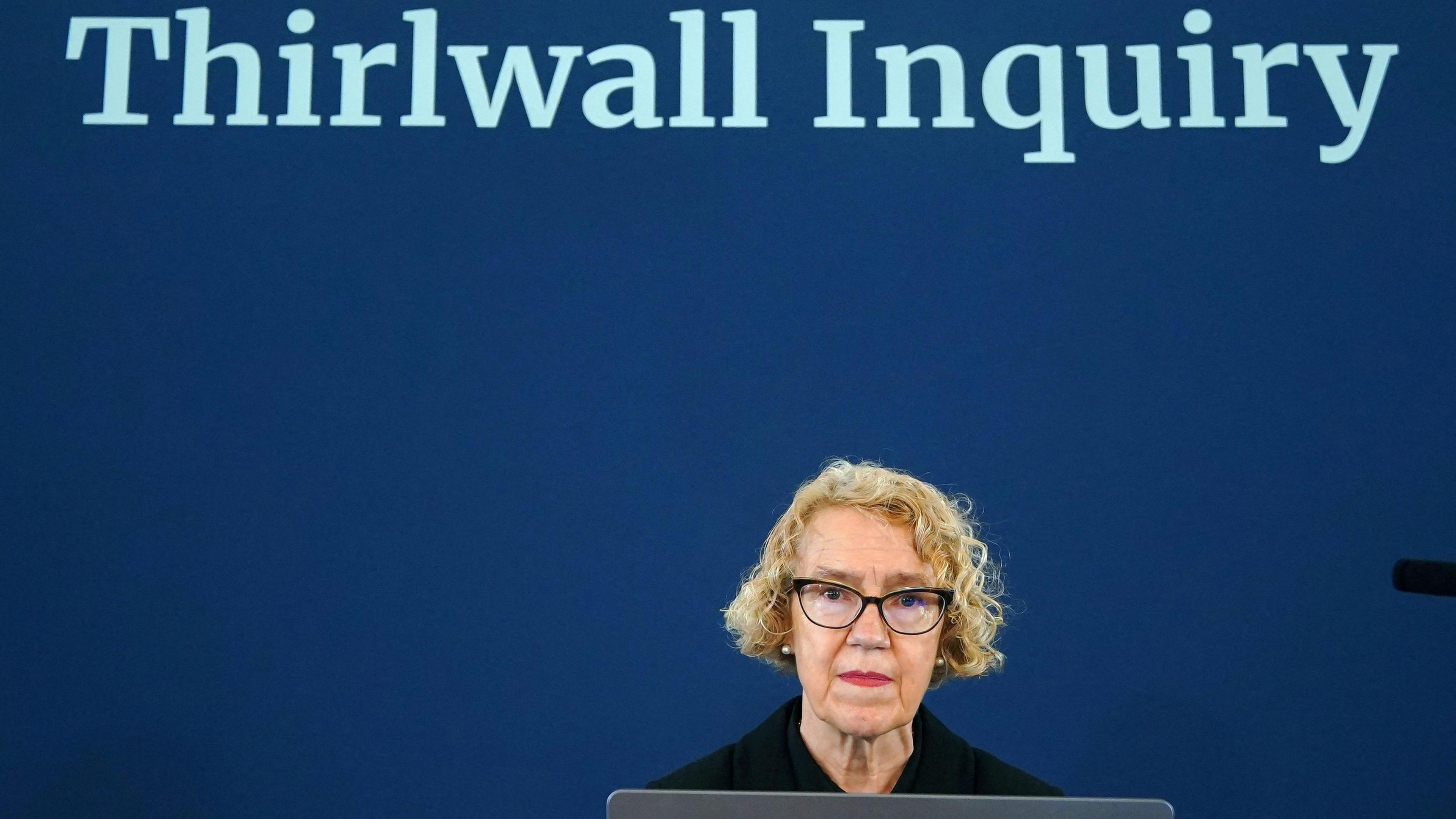 Chair of the inquiry Lady Justice Thirlwall looks on ahead of hearings into the murders and attempted murders of babies by nurse Lucy Letby, at Liverpool Town Hall, in Liverpool. She is dressed in black, has short curly hair and dark rimmed glasses. She sits in front of a laptop and the Thirlwall Inquiry appears above her head on a dark blue background behind her.