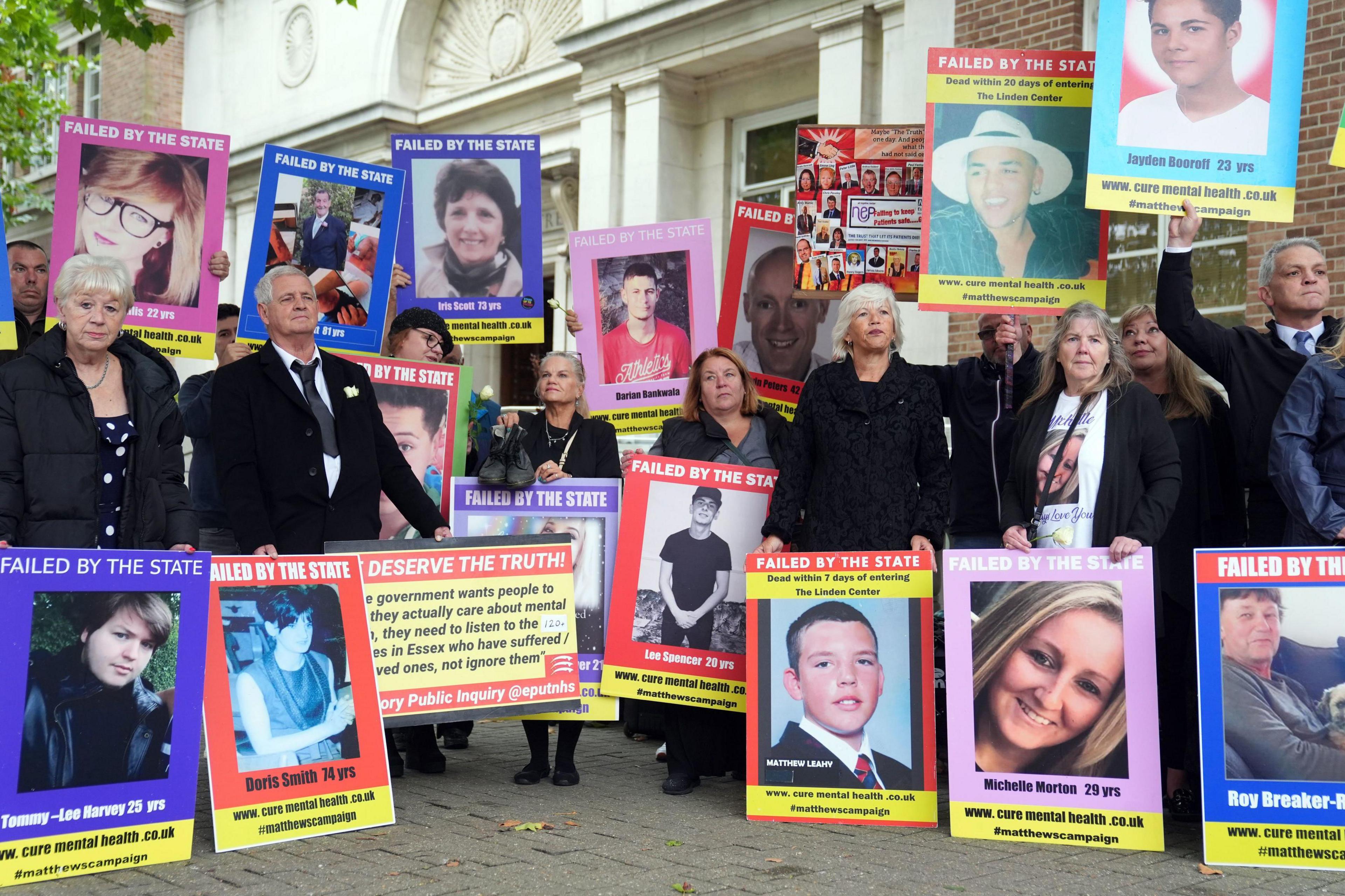 The families of those who have died while in the care of mental health services in Essex stand outside the inquiry protesting. There are about 20 people in the image which shows them standing with placards held against them and large posters of their loved ones. They show a range of faces, both men and women and young and old. One reads "failed by the state".