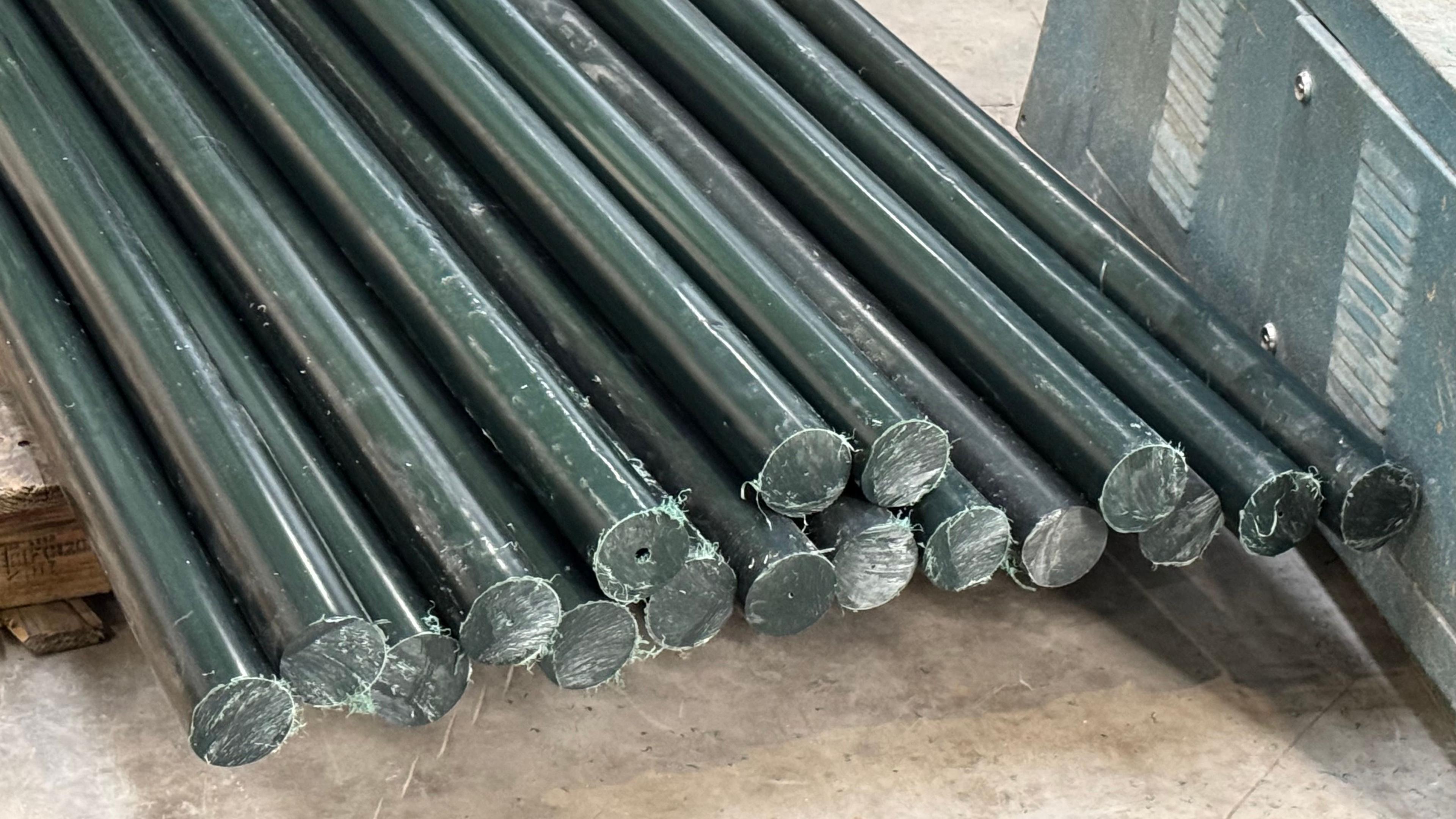 A pile of round black fence posts made out of a plastic-type material lie on factory floor. 