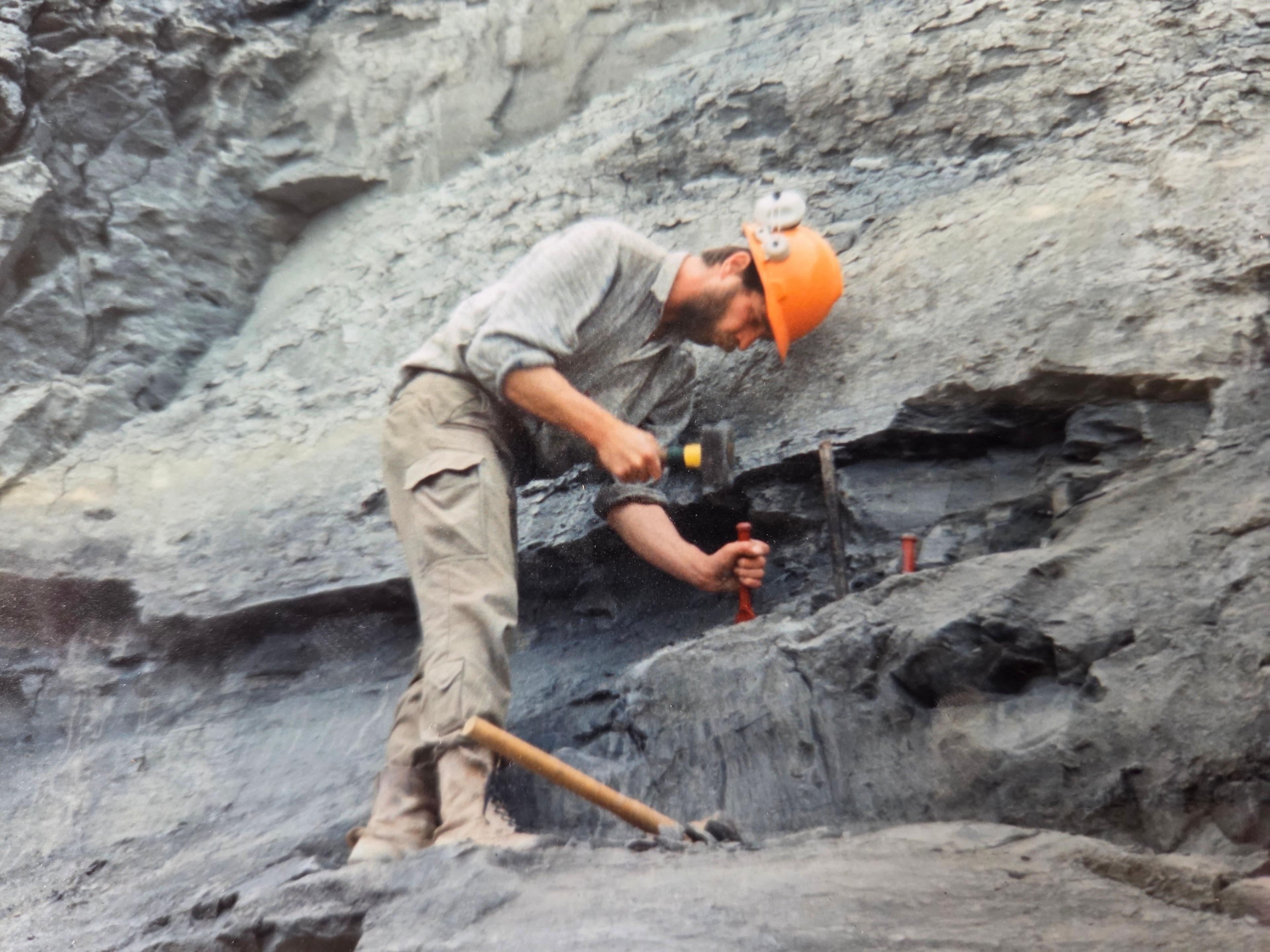 Chris Moore in an orange safety hat chisels at the black cliffs