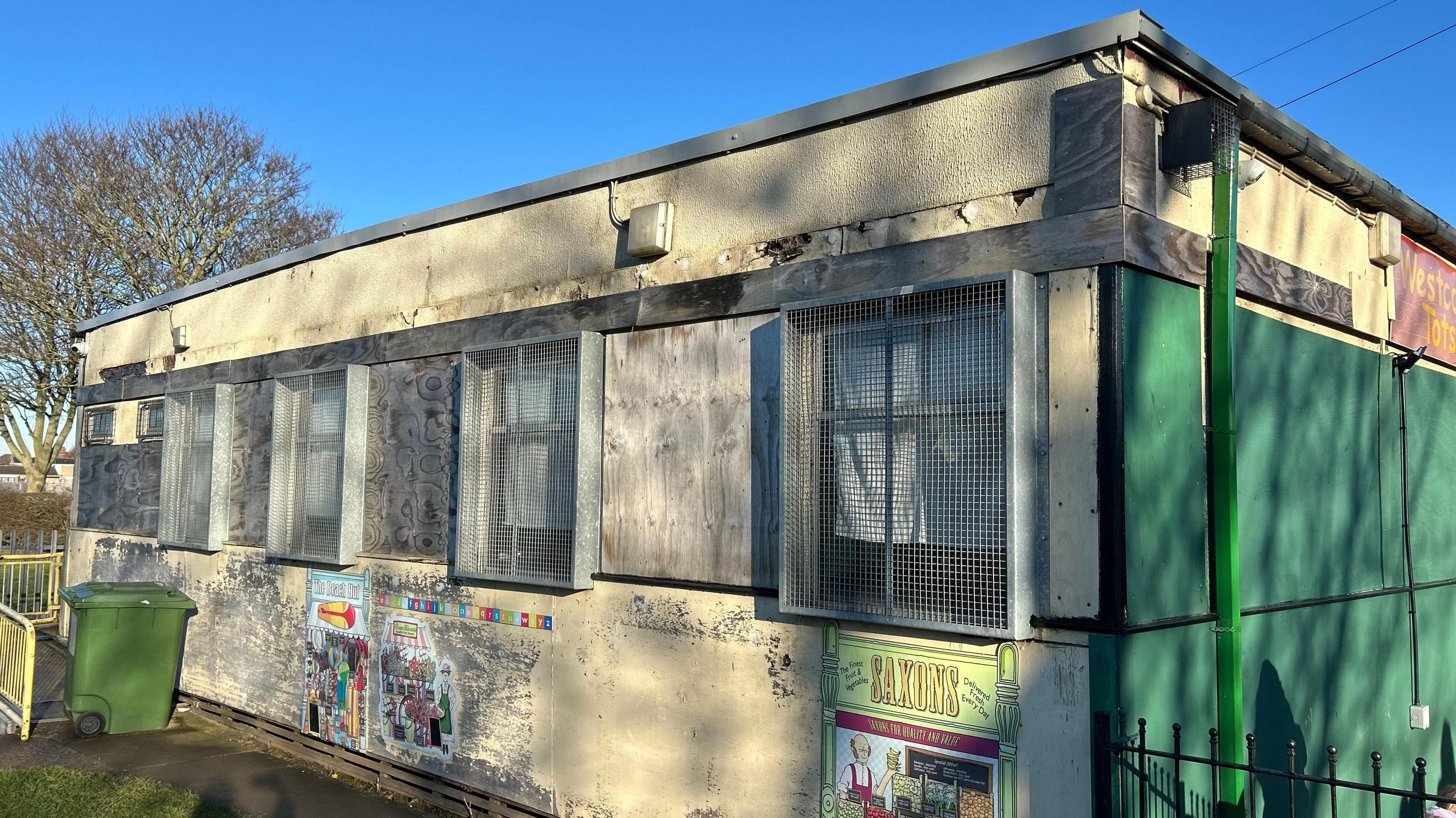 Westcott Totts. A modular building in a state of disrepair. The windows are covered with grills and there are holes in the walls.