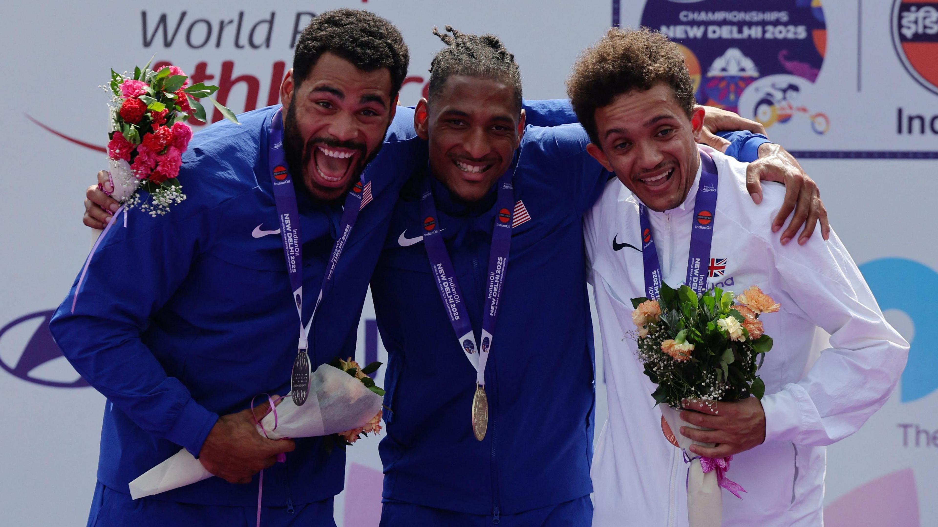 US athletes Jaydin Blackwell and Ryan Medrano pose on the podium alongside Thomas Young with their medal round their neck and holding bunches of flowers