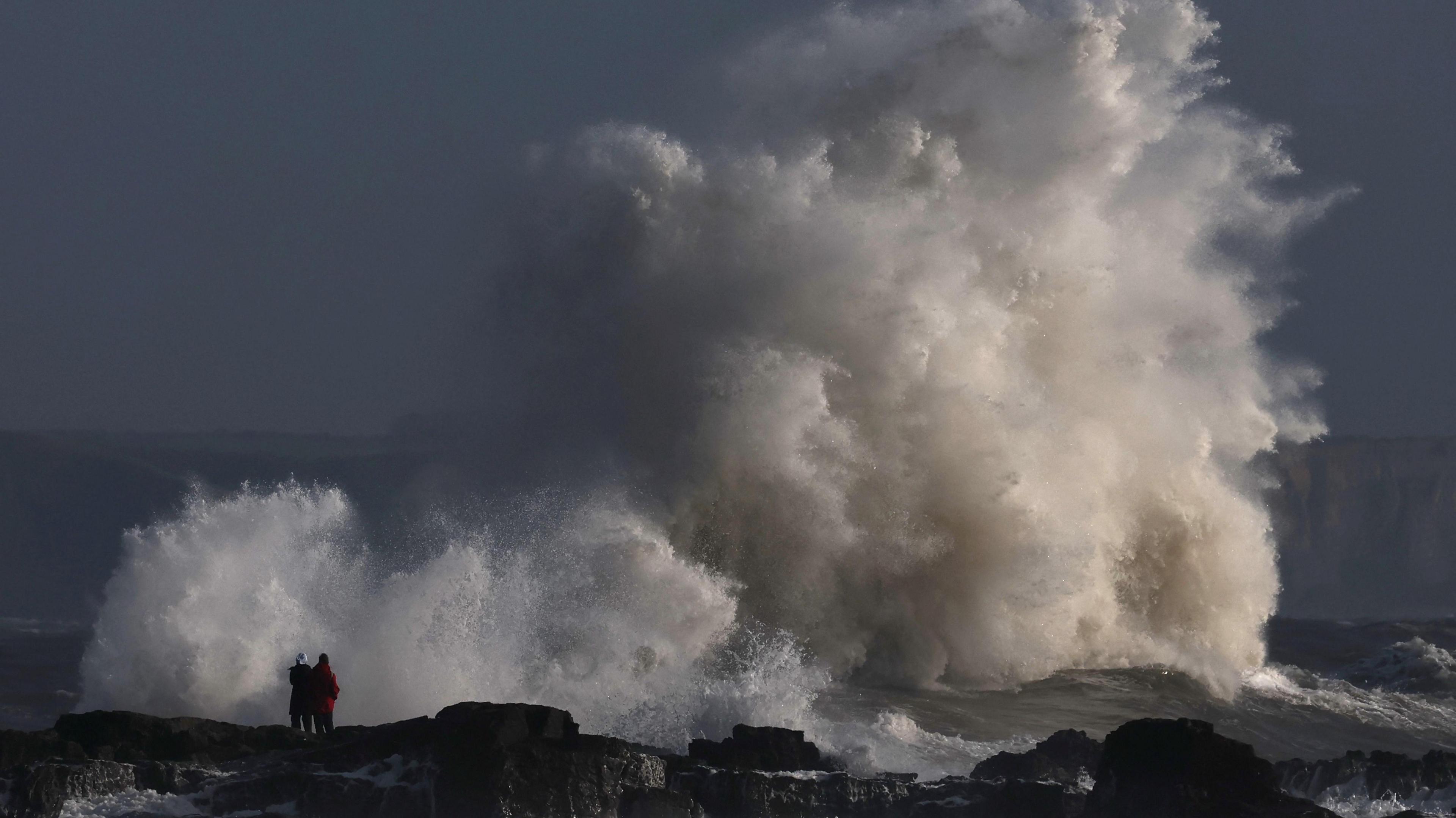 Two people watching a large cloud of sea-spray.