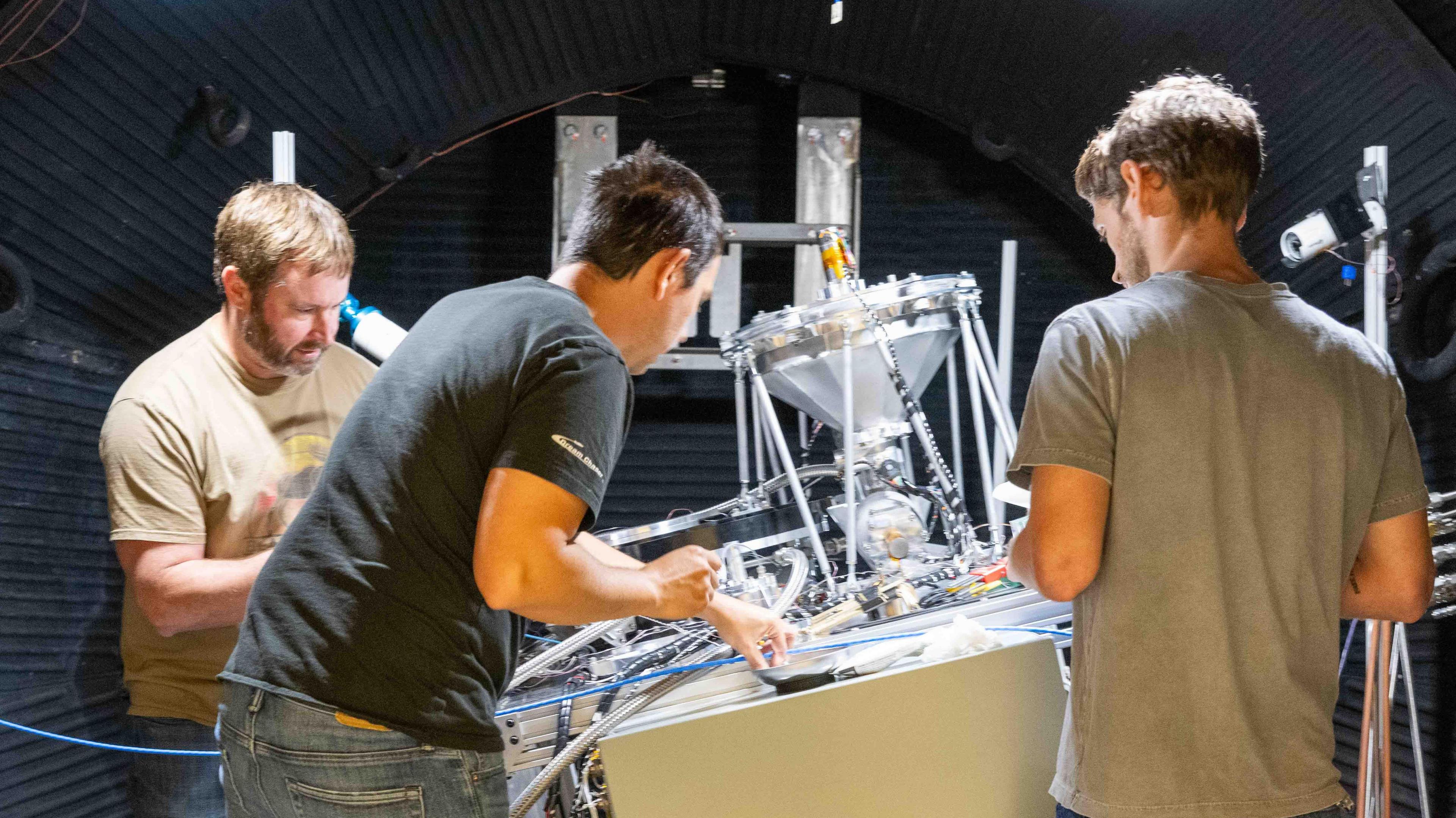 Three Sierra Space engineers work on a machine designed to produce oxygen from a substitute for moon dust