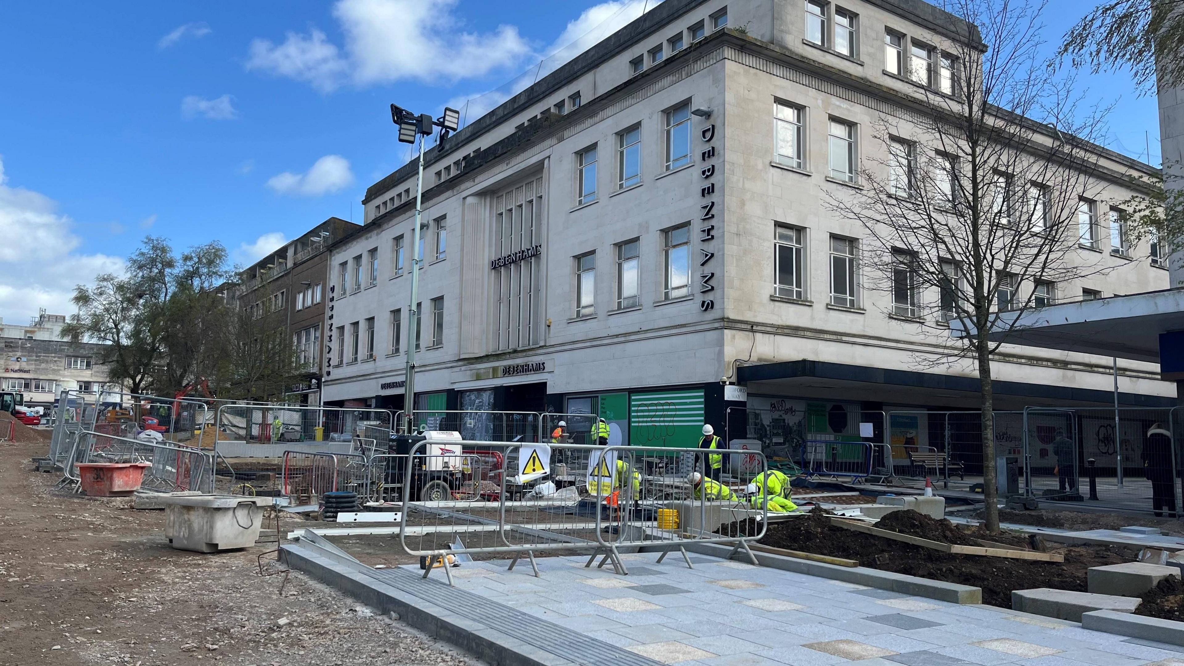 Metal barricades and new paving stones on New George Street in Plymouth with workmen in the background