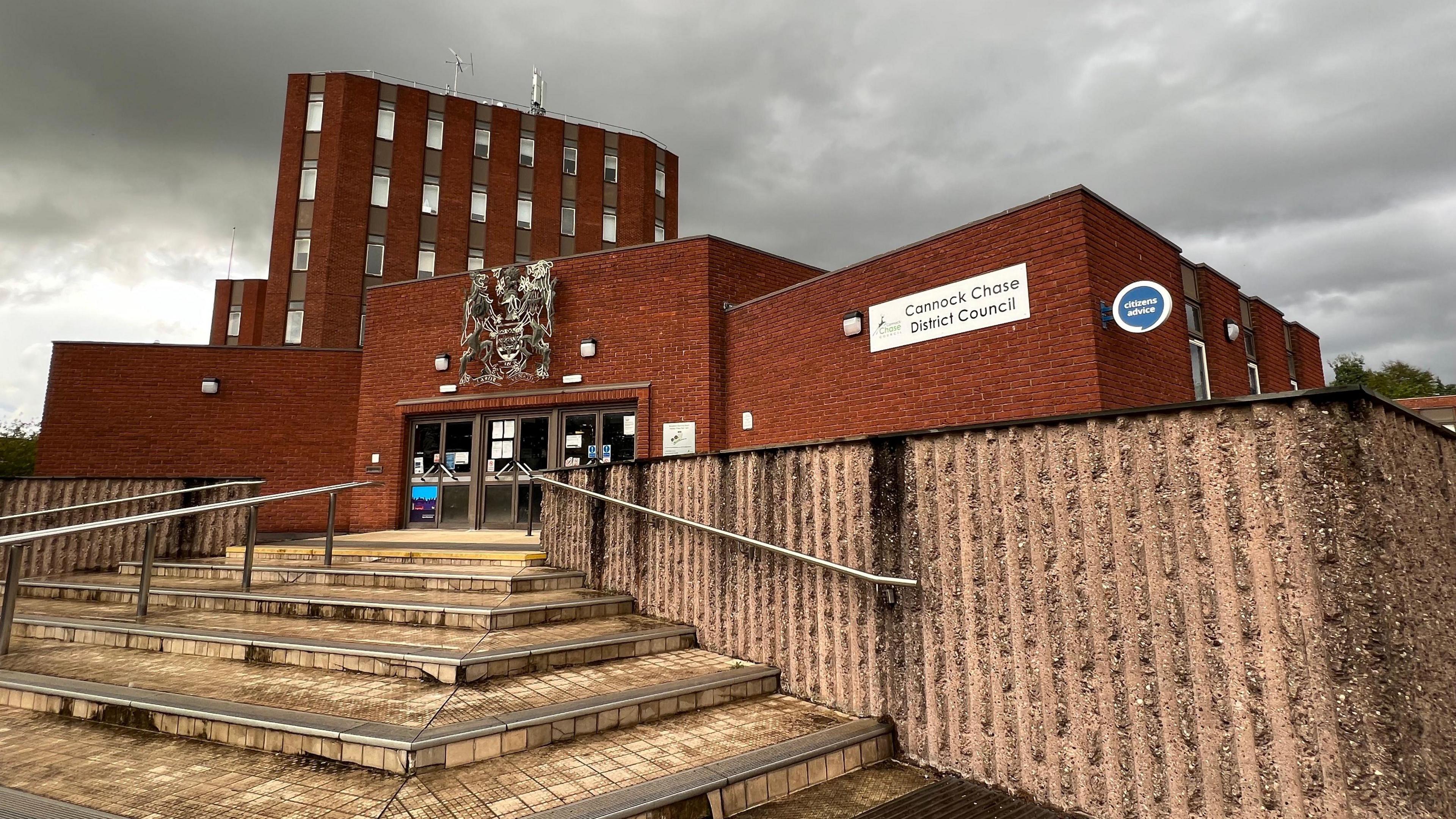 A red-brick council building, with steps leading up to it. There is a large crest above a set of glass doors, and the council logo appears on the side of a section of the building alongside a Citizens Advice logo.