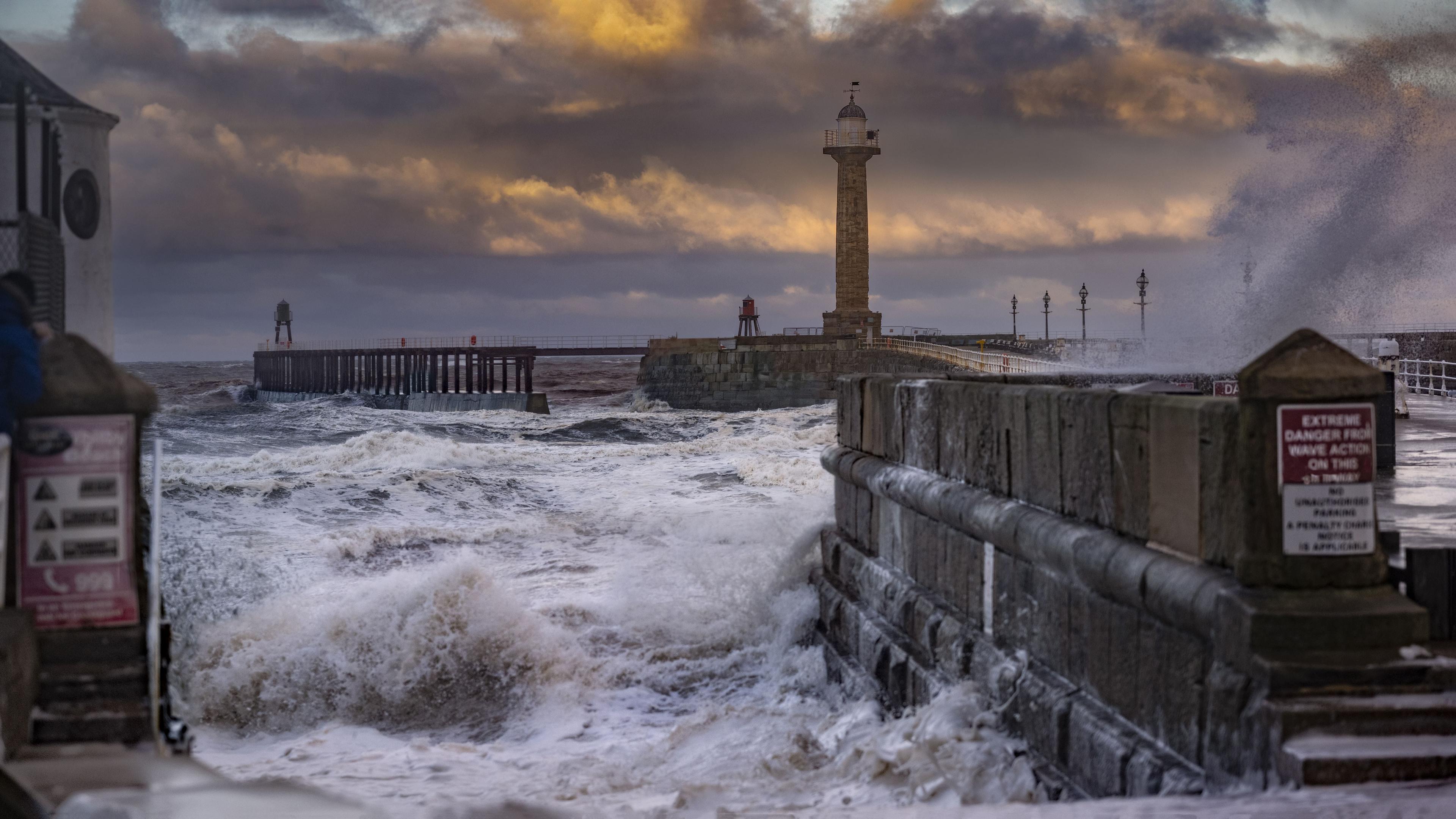 Waves crash against Whitby Harbour against a stormy sky.