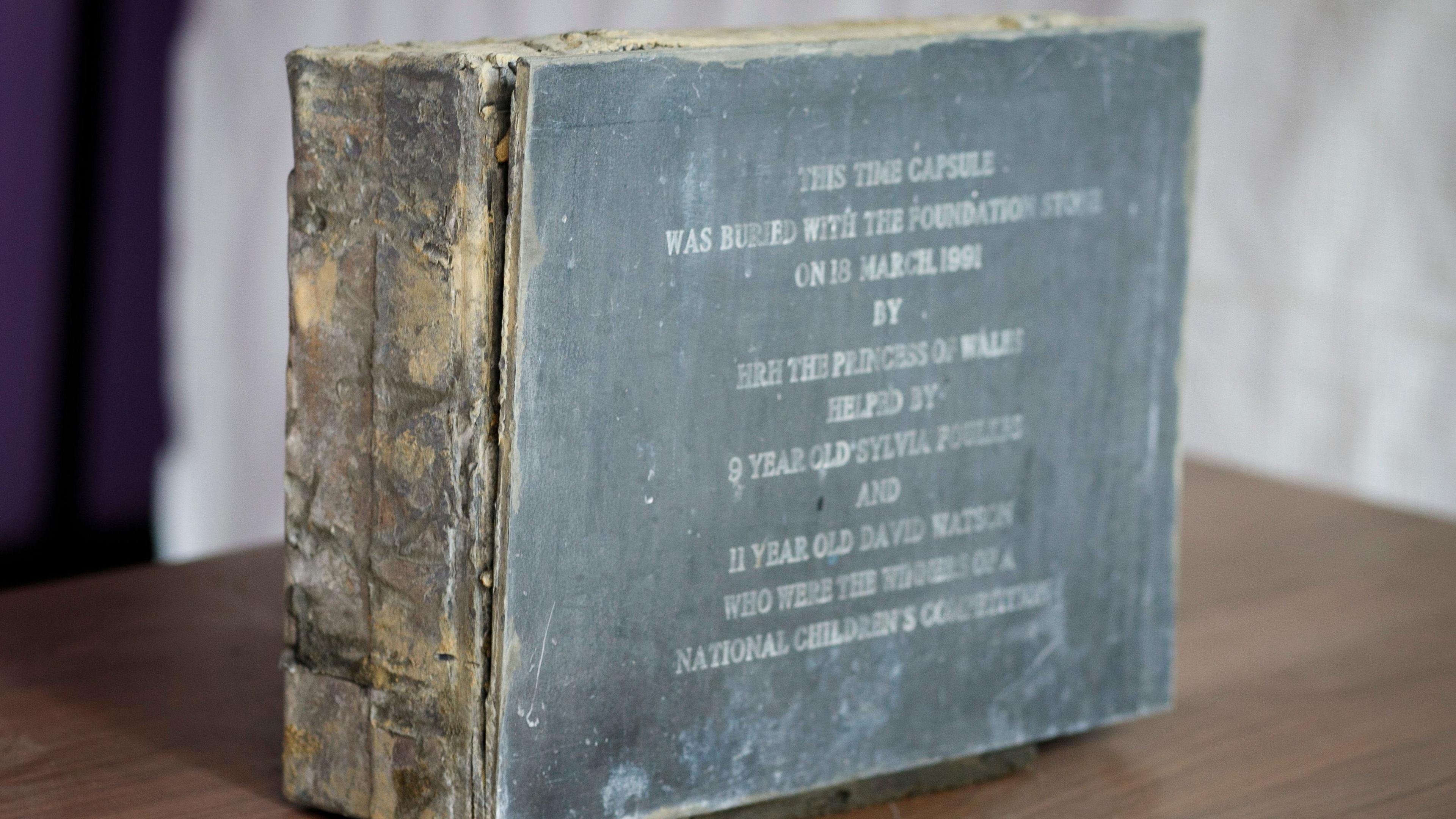 A lead-encased wooden box is on the table. On the outside, there is information written about the date of its burial. 