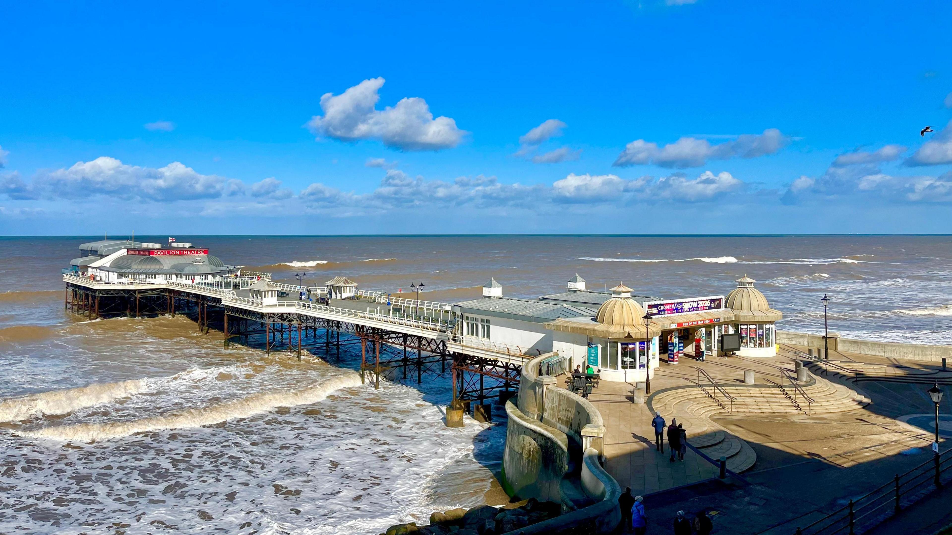 photo of Cromer pier with lots of sunny spells above and with choppy waves beneath